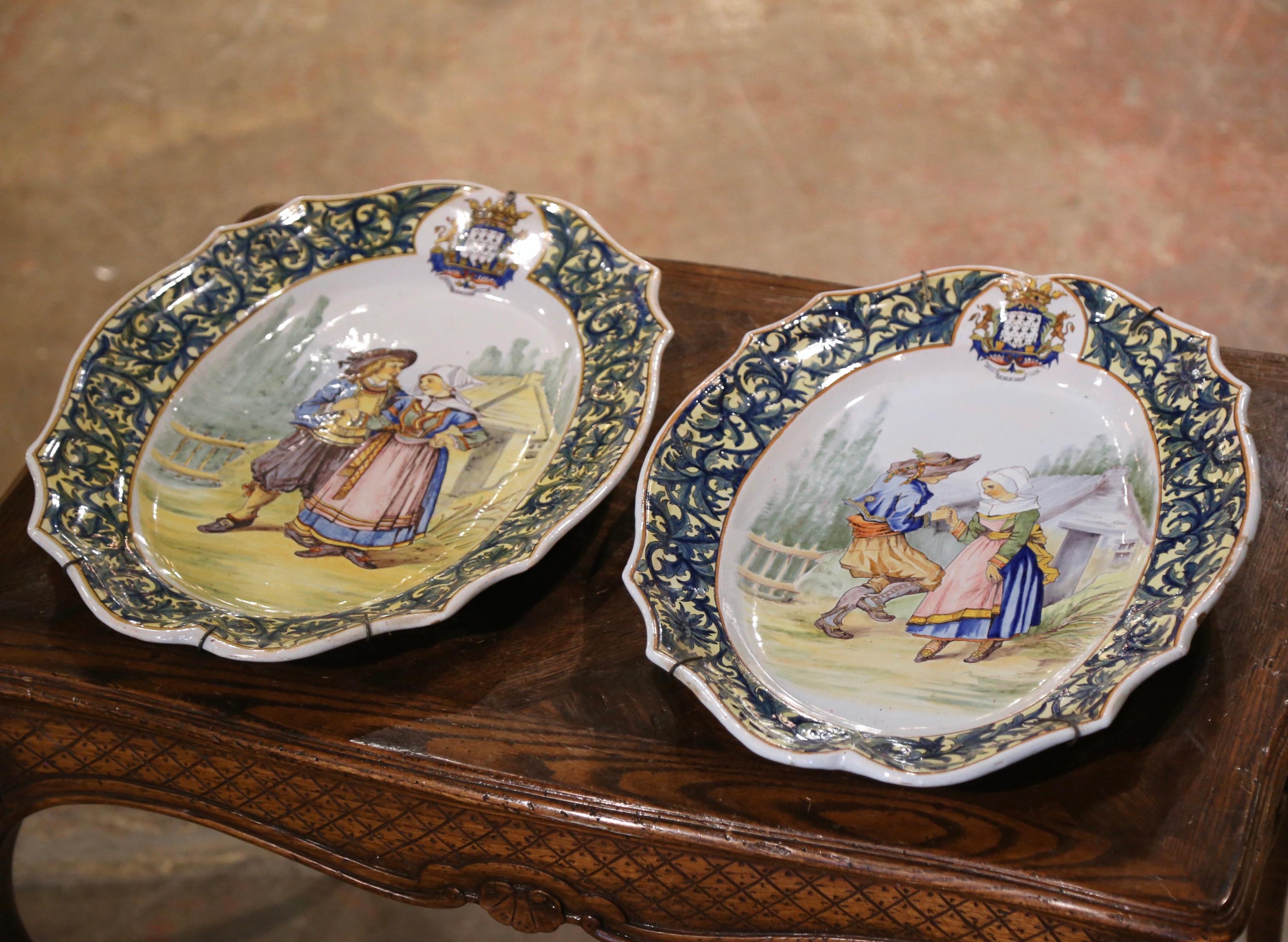 Dekorieren Sie eine Küchenwand oder ein Regal mit diesem wichtigen Paar antiker Teller. Die großen, handbemalten Keramikteller wurden um 1895 von Porquier Beau in Quimper, Frankreich, hergestellt und zeigen traditionelle Werbeszenen mit Bretonen in