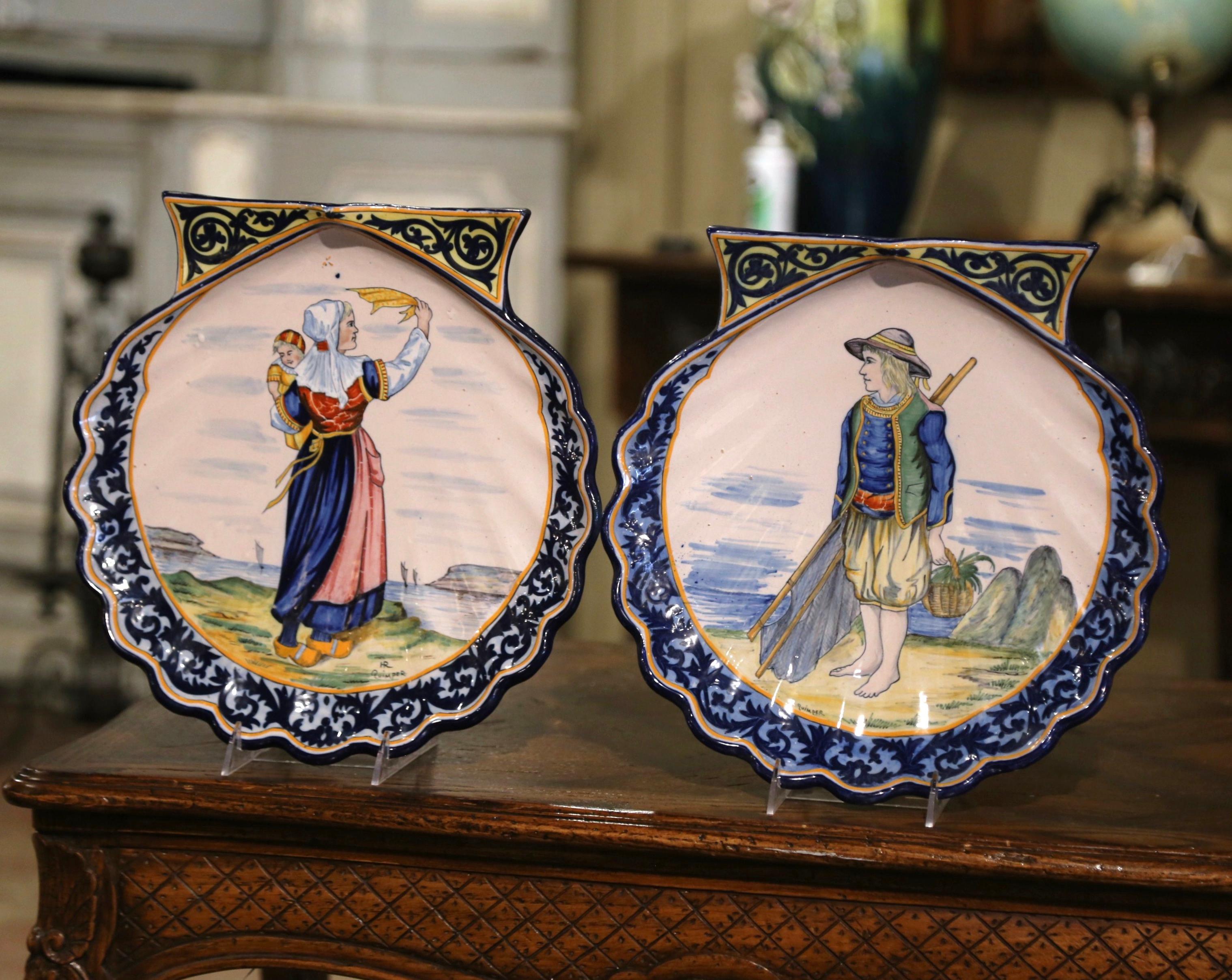 Decorate a kitchen wall or a shelf with this important pair of antique decorative platters. Created in France circa 1910, the large shell-form ceramic plates with scalloped edges, depict typical fishing and coastline scenes with Breton people in