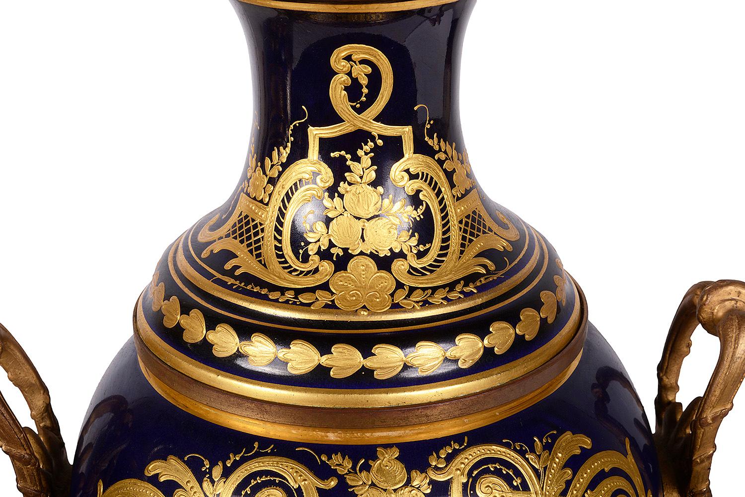 Une paire de vases en porcelaine de style Sèvres de bonne qualité, datant de la fin du 19e siècle, chacun avec des poignées classiques en bronze doré de chaque côté, un fond bleu cobalt avec une décoration dorée, des panneaux peints à la main