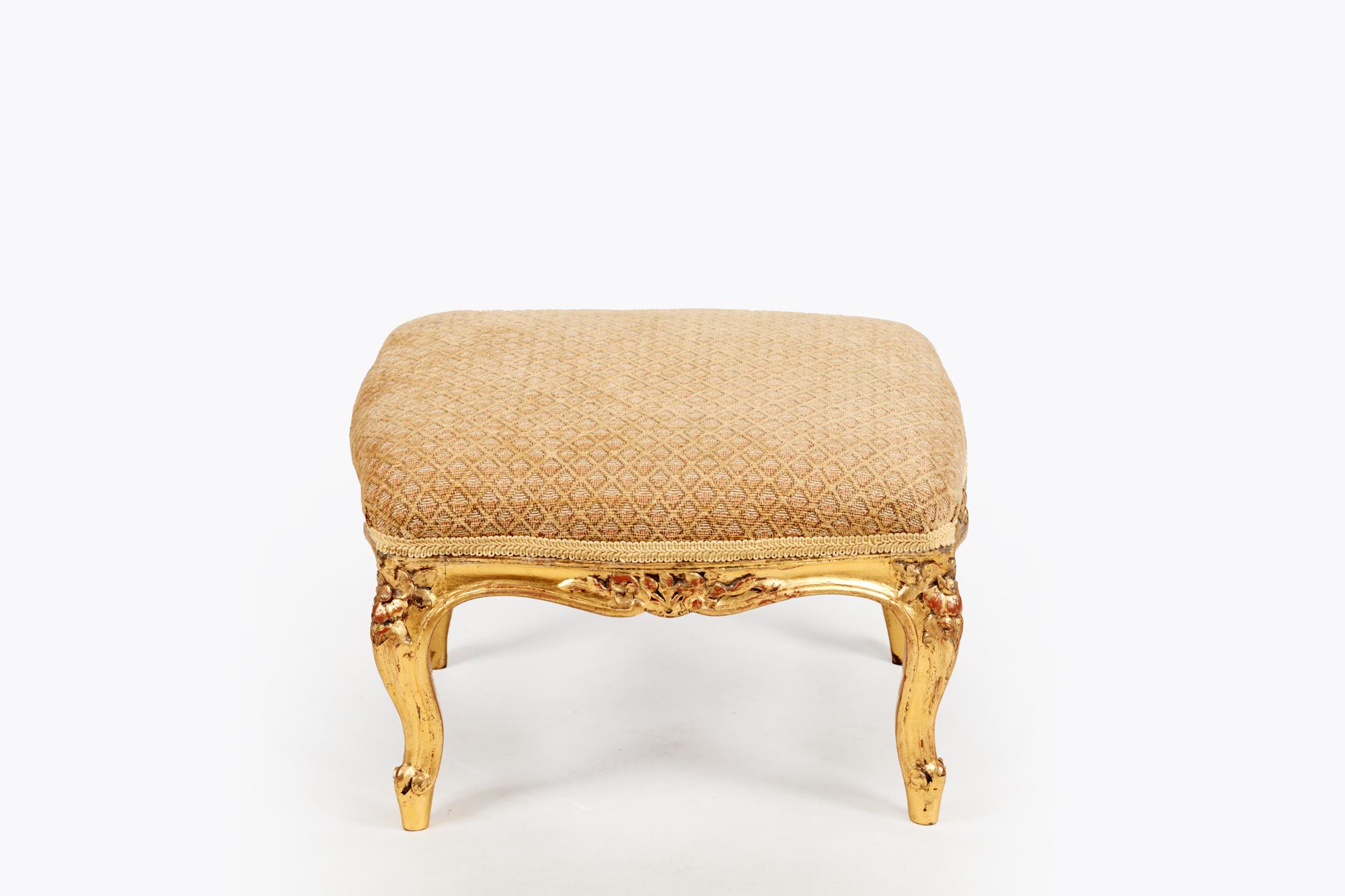 Pair Rococo style giltwood tabourets in rectangular form with foliate carving throughout, raised on cabriole legs terminating on scrolled feet over intricate bow aprons. These stools have a rich gilt patinated finish which is trimmed by decorative