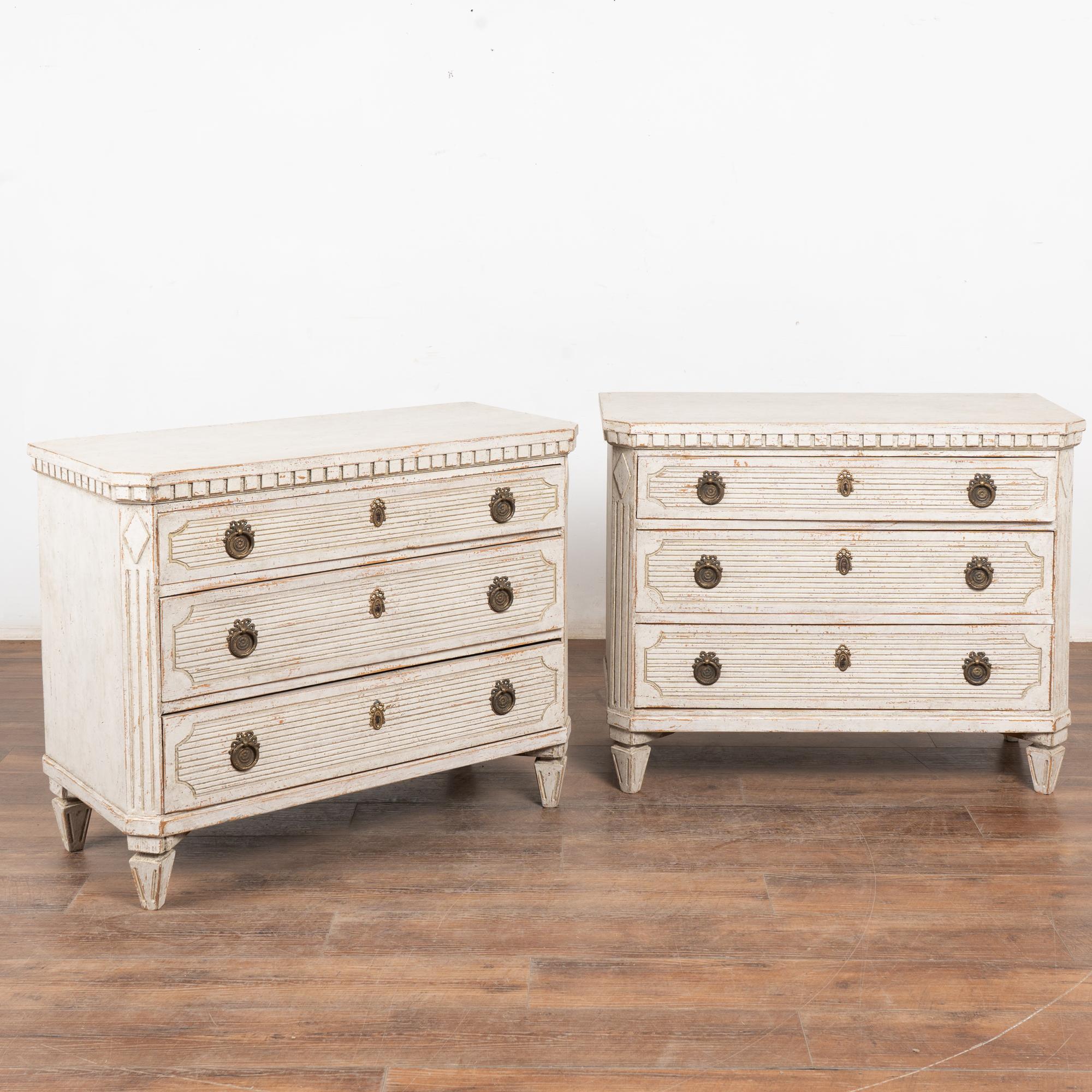 Coppia di cassettiere decorative in pino gustaviano dipinte con tonalità di  bianco, in linea con la loro origine svedese.
Montanti laterali scanalati inclinati con medaglione superiore a diamante intagliato, dettagli scanalati intagliati lungo i