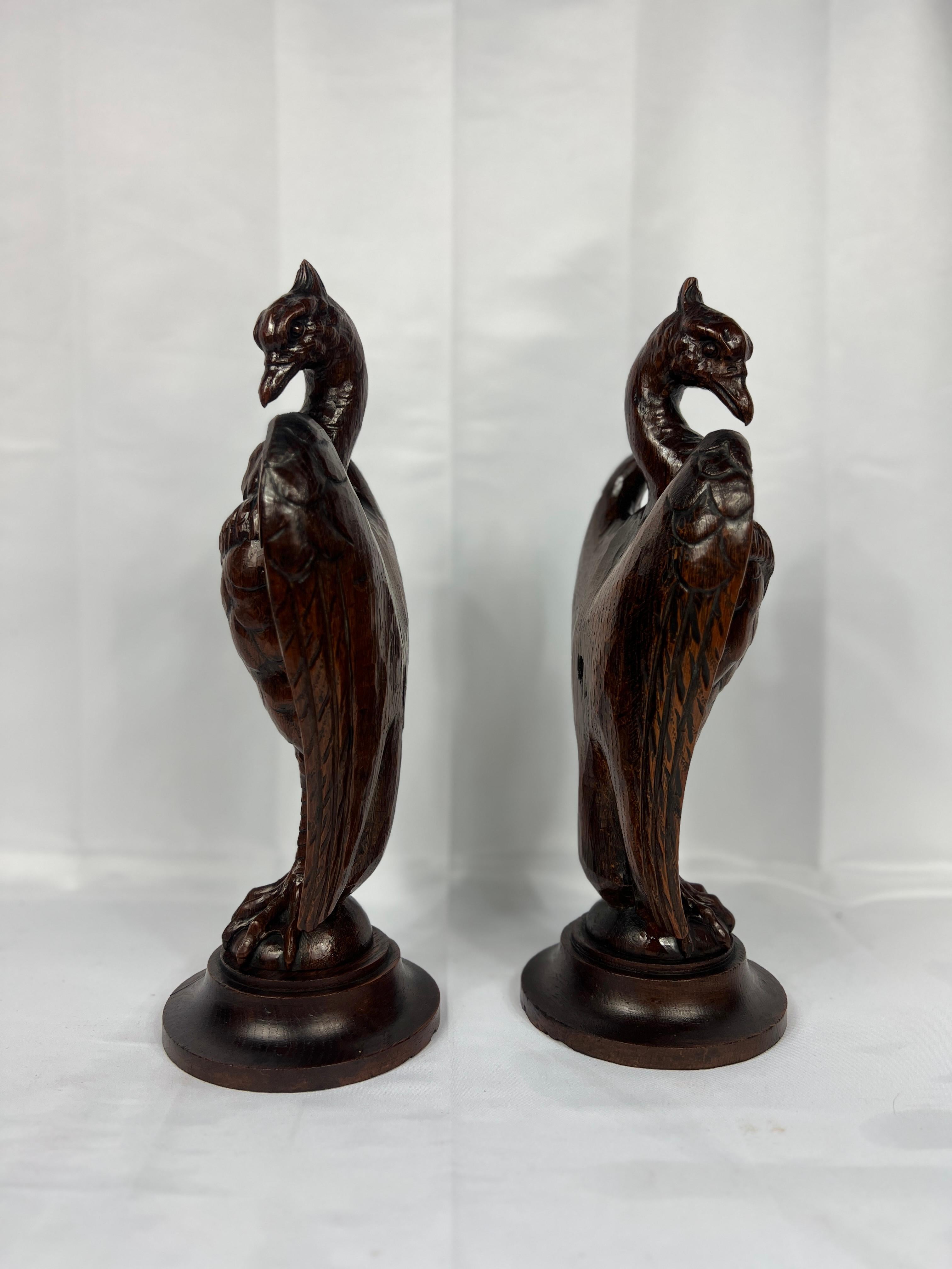 This striking pair of antique newel post finials features finely hand-carved wooden eagles, embodying the grandeur and craftsmanship of the late 19th to early 20th century. Each eagle is depicted in a majestic pose, with wings partially extended and