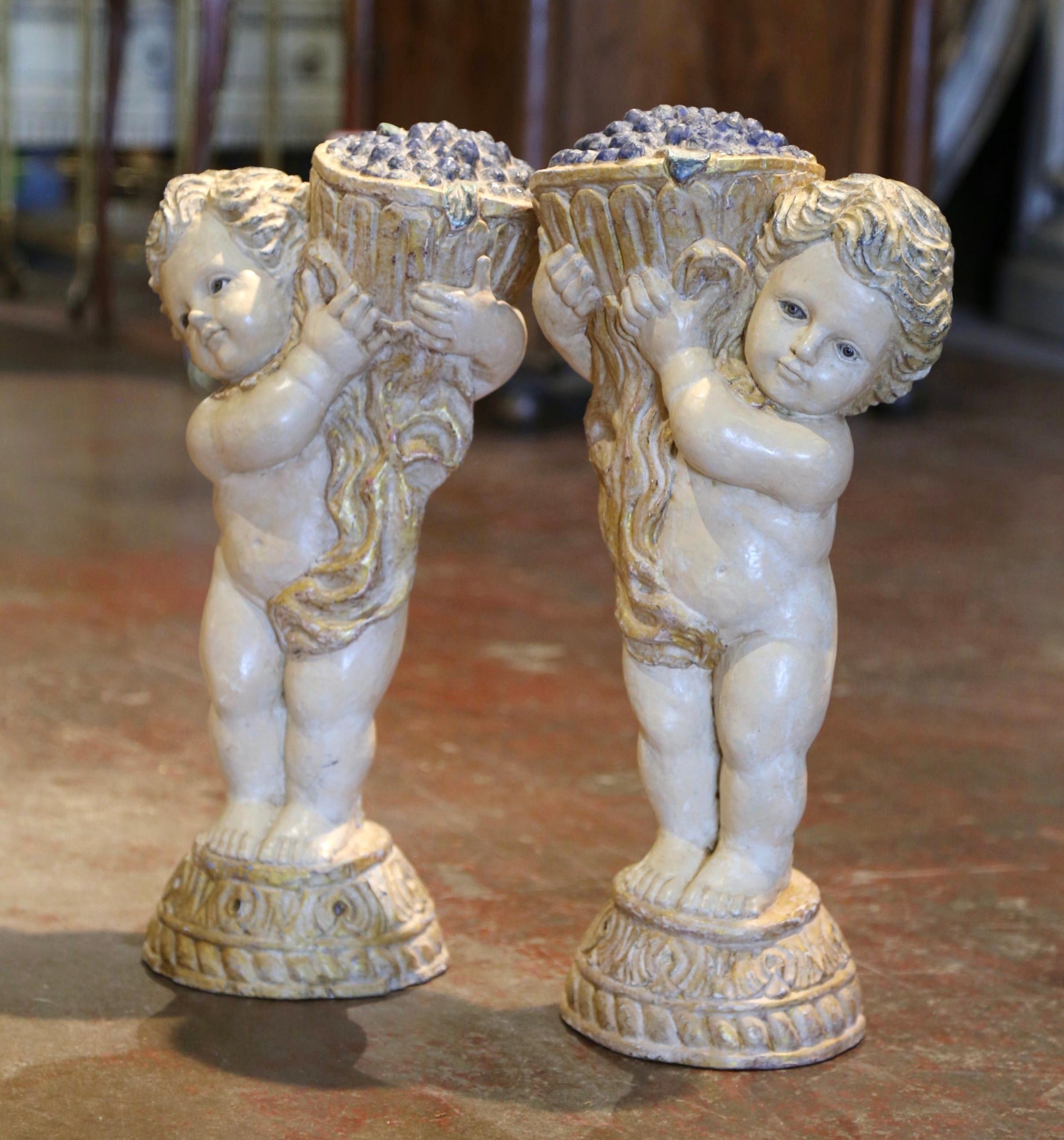 Elegia una cantina o un bar con questa elegante coppia di sculture di cherubini antichi, con il bambino Bacco, dio del vino, che rappresenta la vendemmia e il piacere del vino! Realizzato in Italia intorno al 1850, ogni bambino paffuto e colorato,
