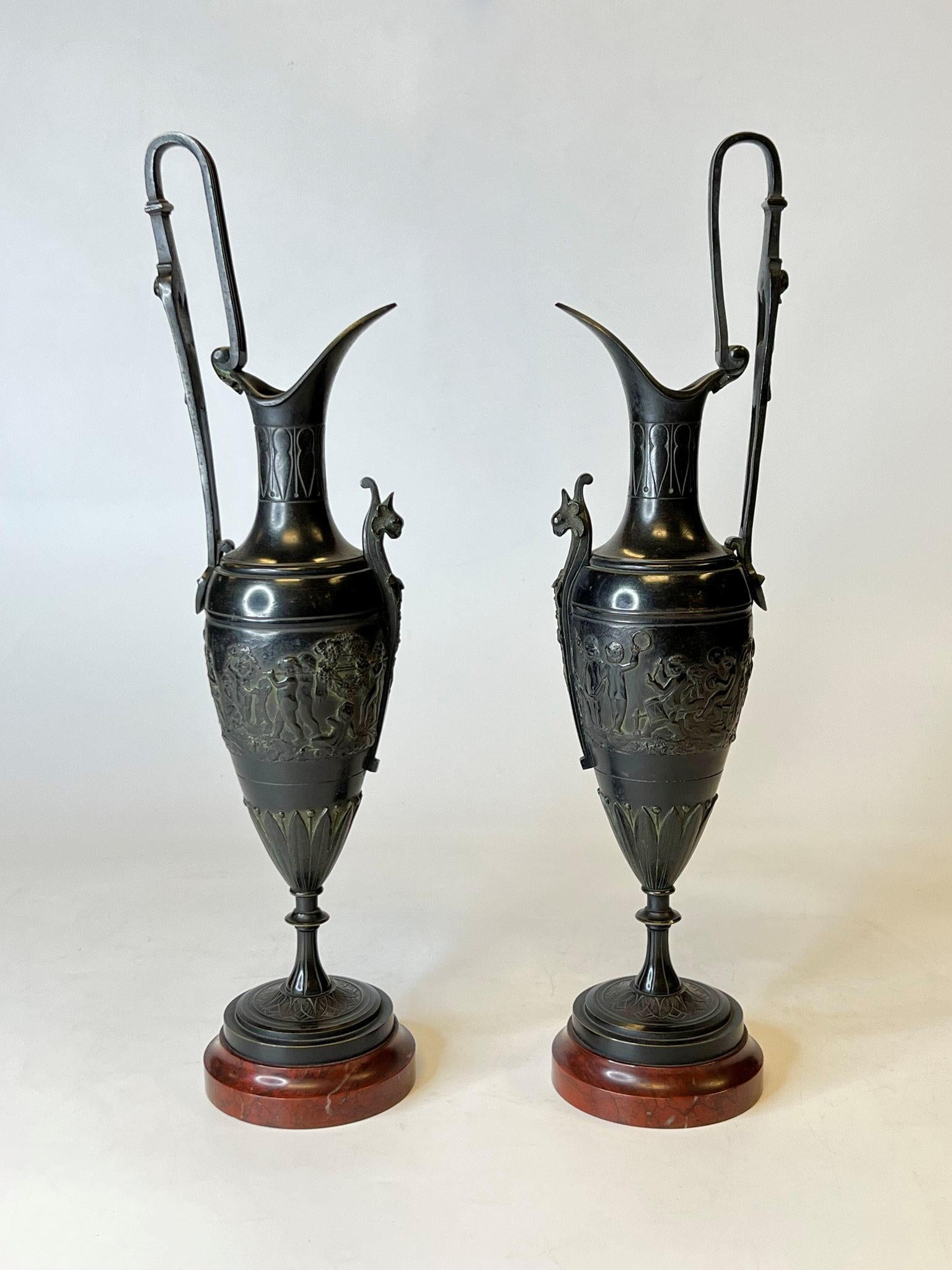 Pair of 19th century patinated bronze ewers of the finest quality in the Roman or Greco-Roman style depicting frolicking cherubs (putti) in a Bacchanal scene, likely of Italian or possibly French origin. 