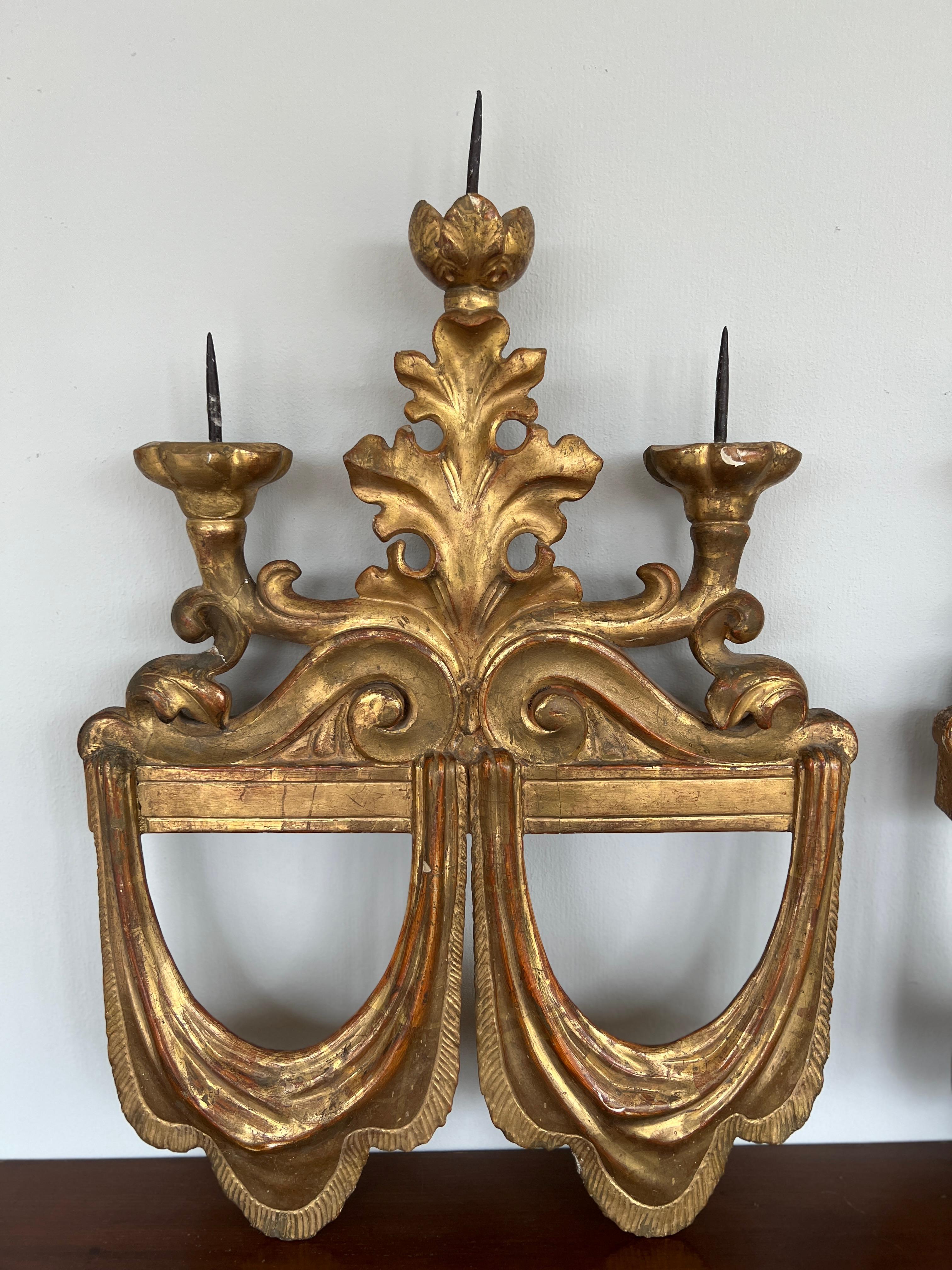 Italy, circa 1890.

A pair of antique giltwood 3-light candle sconces. Each sconce features finely detailed and hand carved rococo style candelabra arms, supporting sharp iron prickets. Highly detailed and realistic double draped water gilt hangings