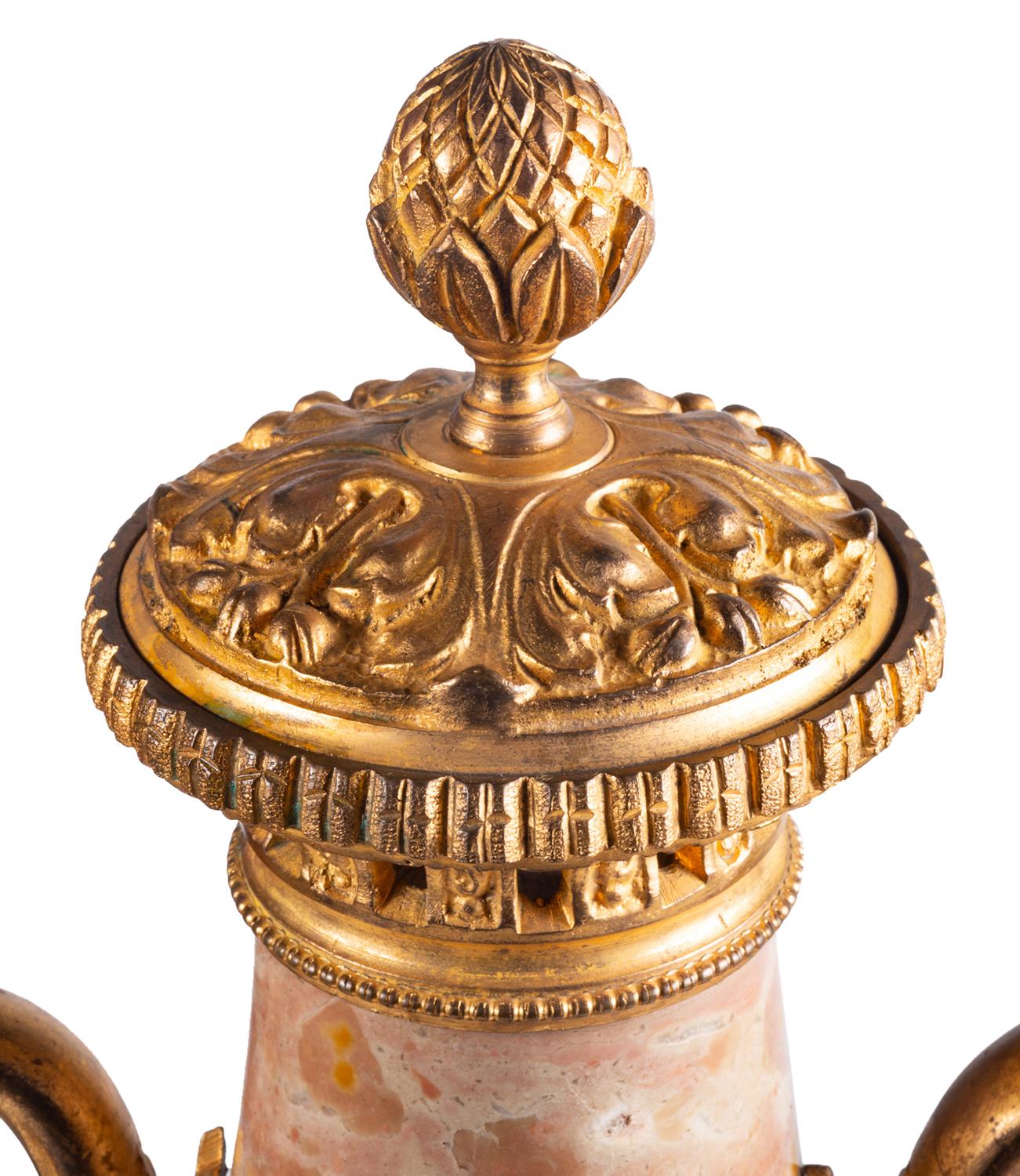 A good quality pair of late 19th century, Louis XVI style rouge marble, lidded urns each with classical gilded ormolu mounts of scrolling foliate and floral swags, ribbons and swans head handles and raised on pedestal bases.