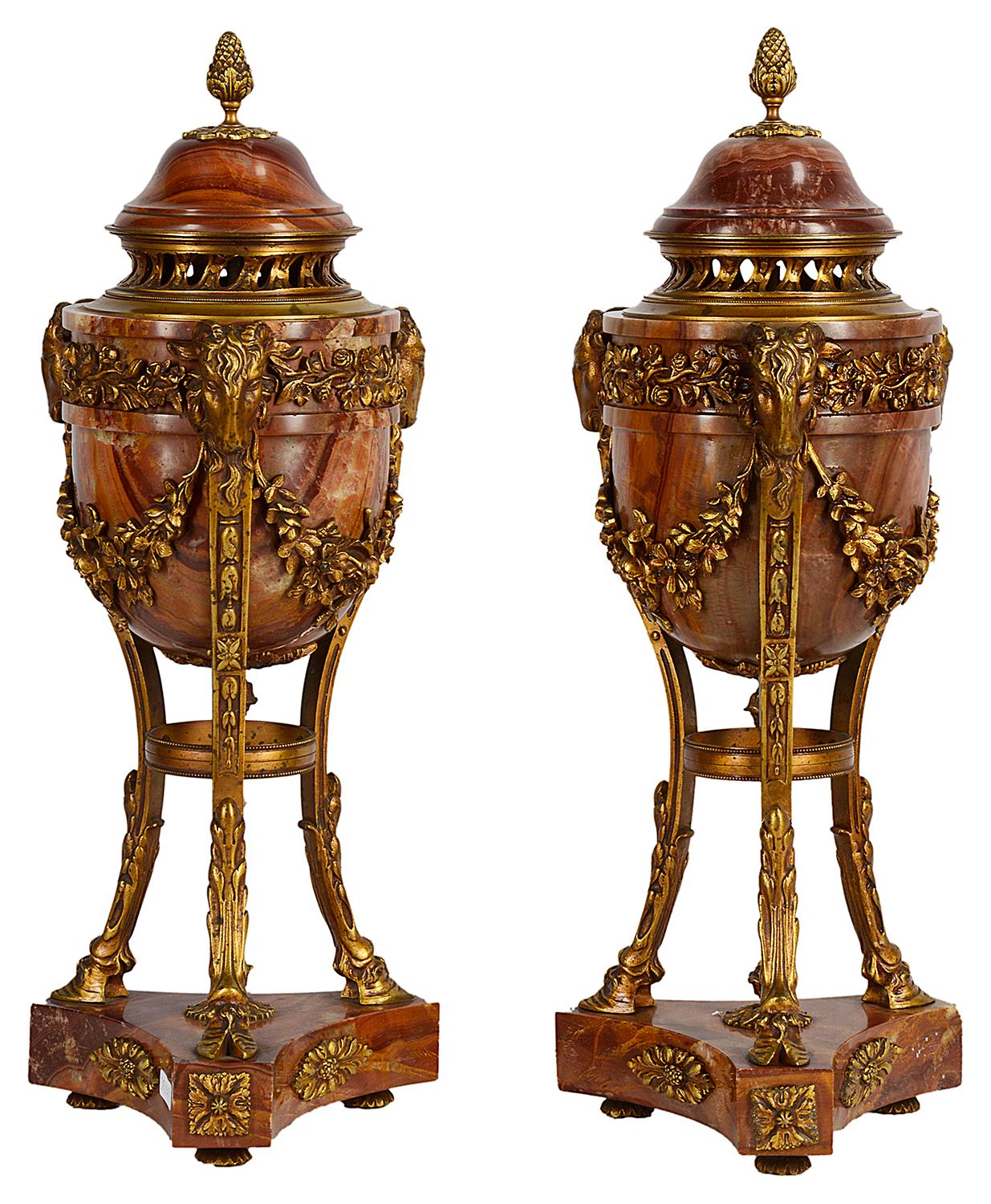 A good quality pair of late 19th century French marble and gilded ormolu urns, each with classical Rans head mounts, supported by three out-swept supports, terminating in hoof feet and raised on a marble plinths.