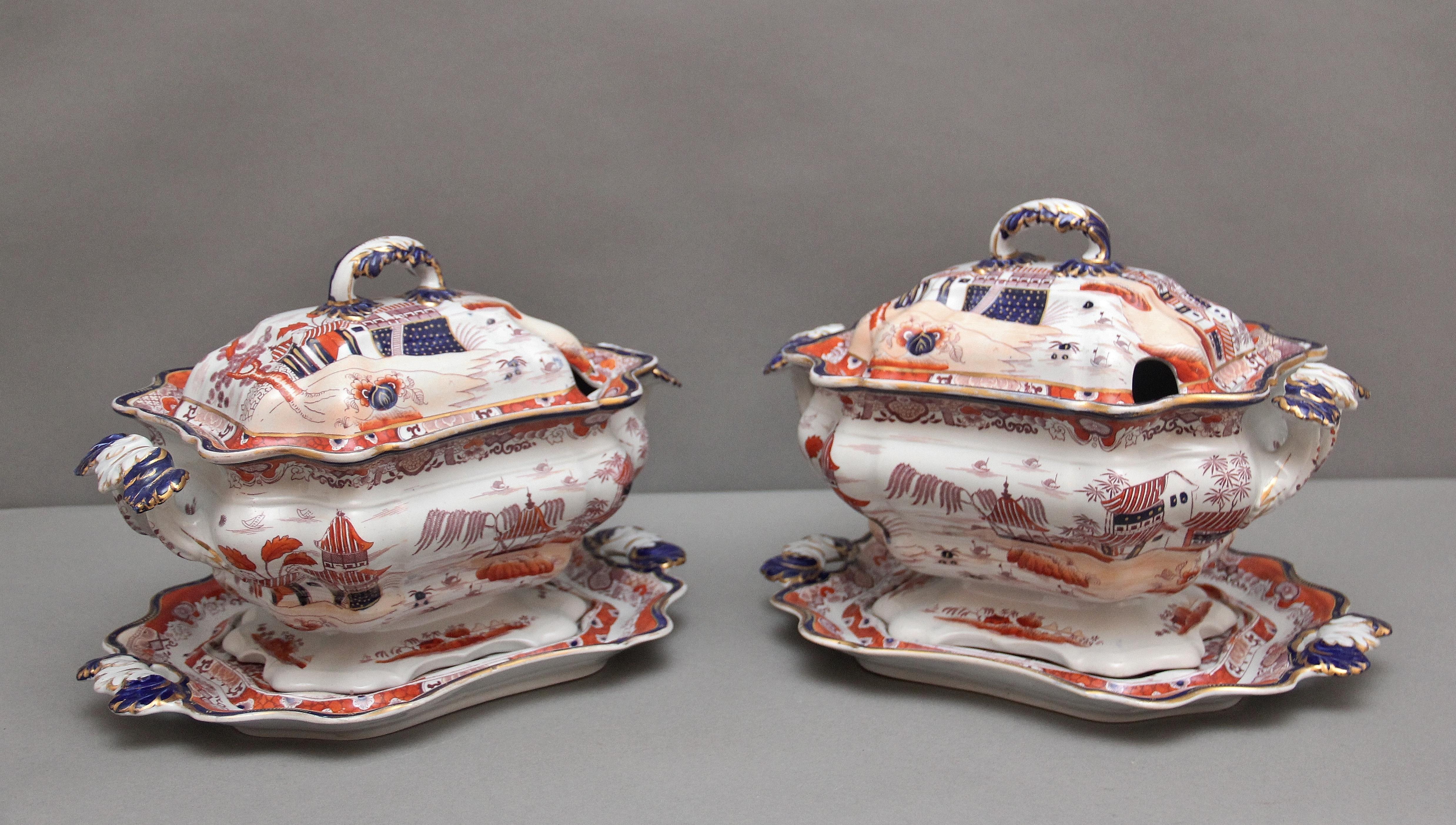 A highly decorative pair of 19th Century Mason's iron stone tureens with a Japanese chinoiserie pattern, having a dome covered lid with a decorative shaped handle, the shaped bowl with elegant shaped handles either end and resting on a shaped tray,