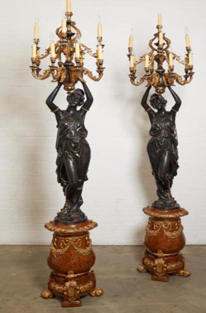 Both are modelled as robed female figures holding aloft thirteen scrolled candlearms, on marbleized bronze plinths hung with ribbons and fruiting garlands, on pawfeet. After Albert-Ernest Carrier-Belleuse (1824 - 1887).

They have been electrified.