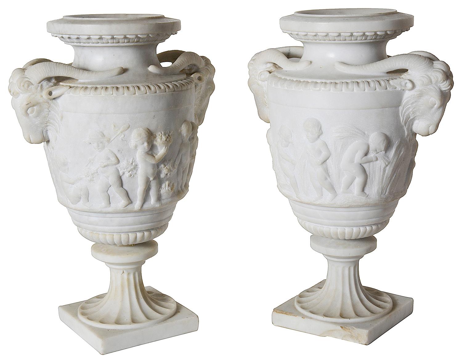 A fine quality pair of late 19th century carved Carrera marble neoclassical urns, each depicting the children gathering the harvest, flowers and with rams head handles on either side.