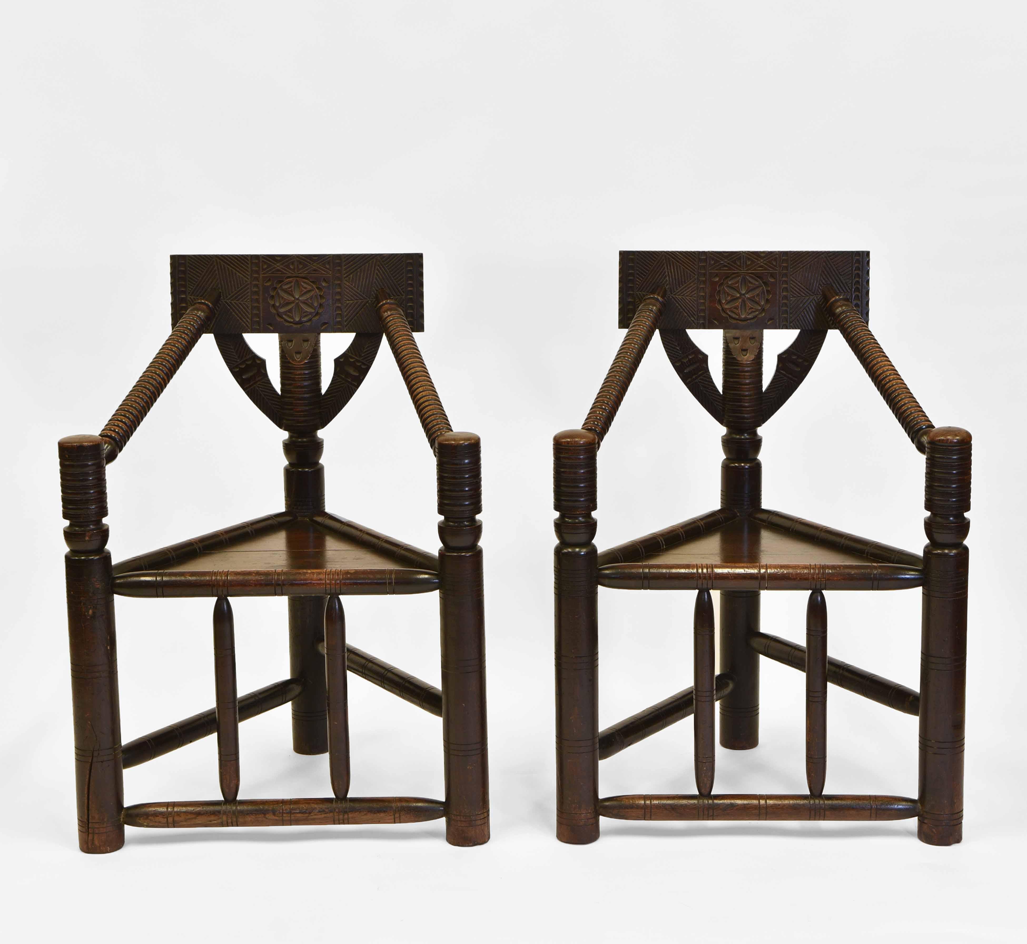 A pair of antique Arts & Crafts period three-legged oak turner's chairs in an early English manner. Circa 1880.

These beautiful hand-crafted chairs made in solid oak have a linear and sculptural feel, with chip carving and geometric incised