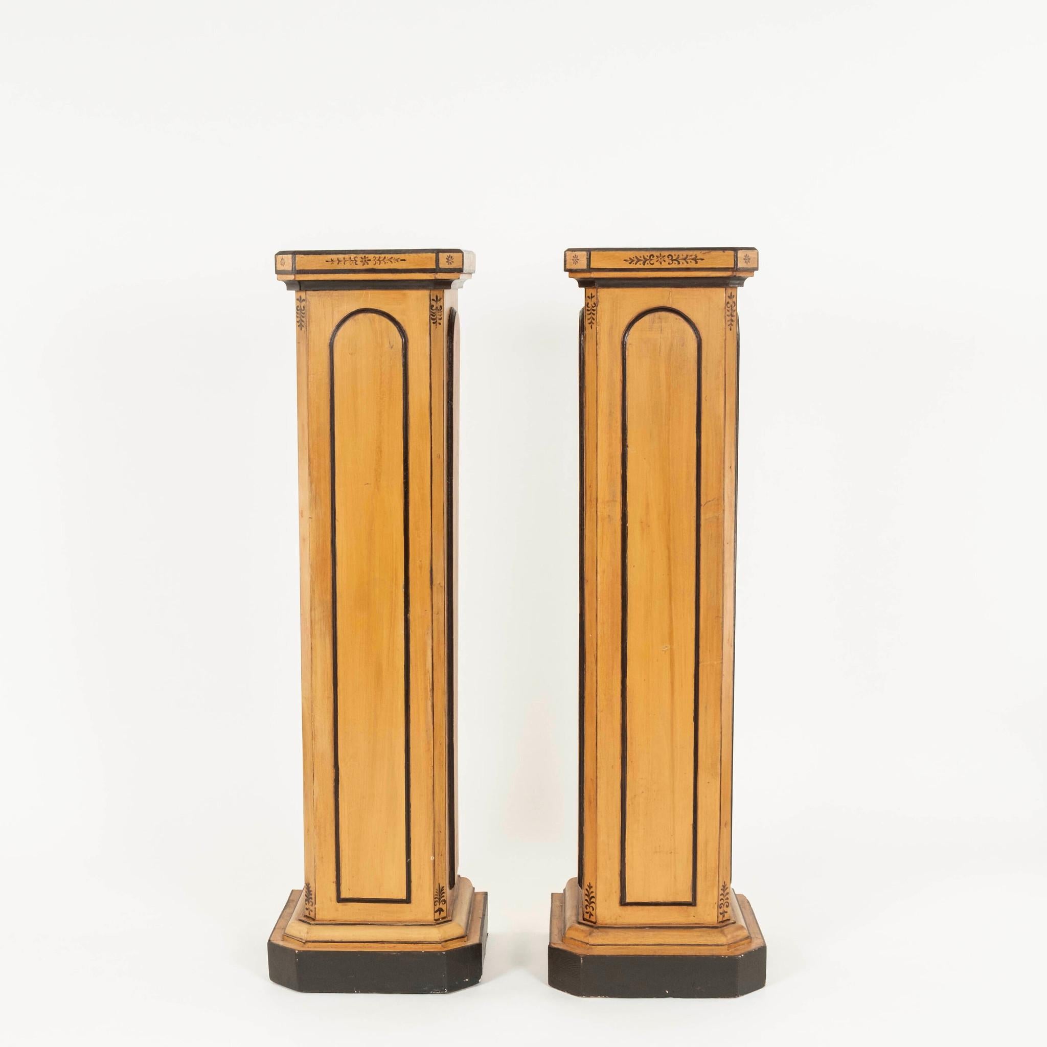 A pair of 19th Century French Charles X painted wood column pedestals. This lovely pair features arched raised panels accented with dark painted trim detail.