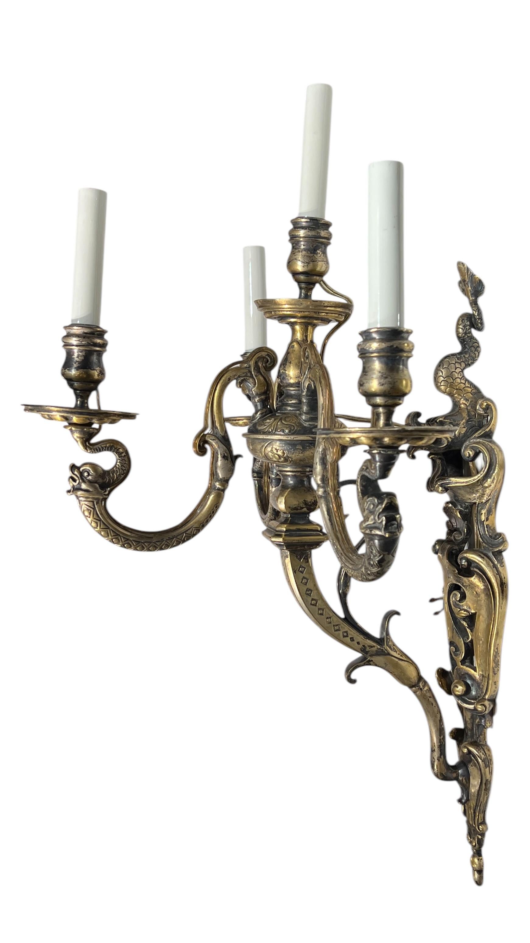 Paire de grandes appliques anciennes (fin du XIXe siècle) en bronze argenté de style Renaissance avec quatre bras de bougie électrifiés, avec plaque murale à motifs de volutes ajourées et dauphin stylisé proéminent au sommet.  Chacune mesure 27 x 17