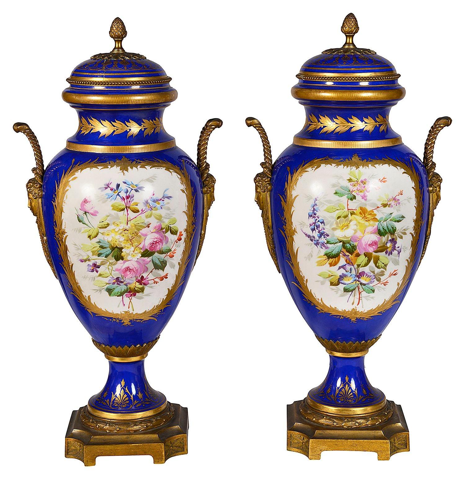 Paire de vases à couvercle en porcelaine de style Sèvres avec montures en bronze doré, chacun avec un fond bleu cobalt, un décor de feuillage doré, des panneaux peints à la main représentant des scènes romantiques et reposant sur des bases