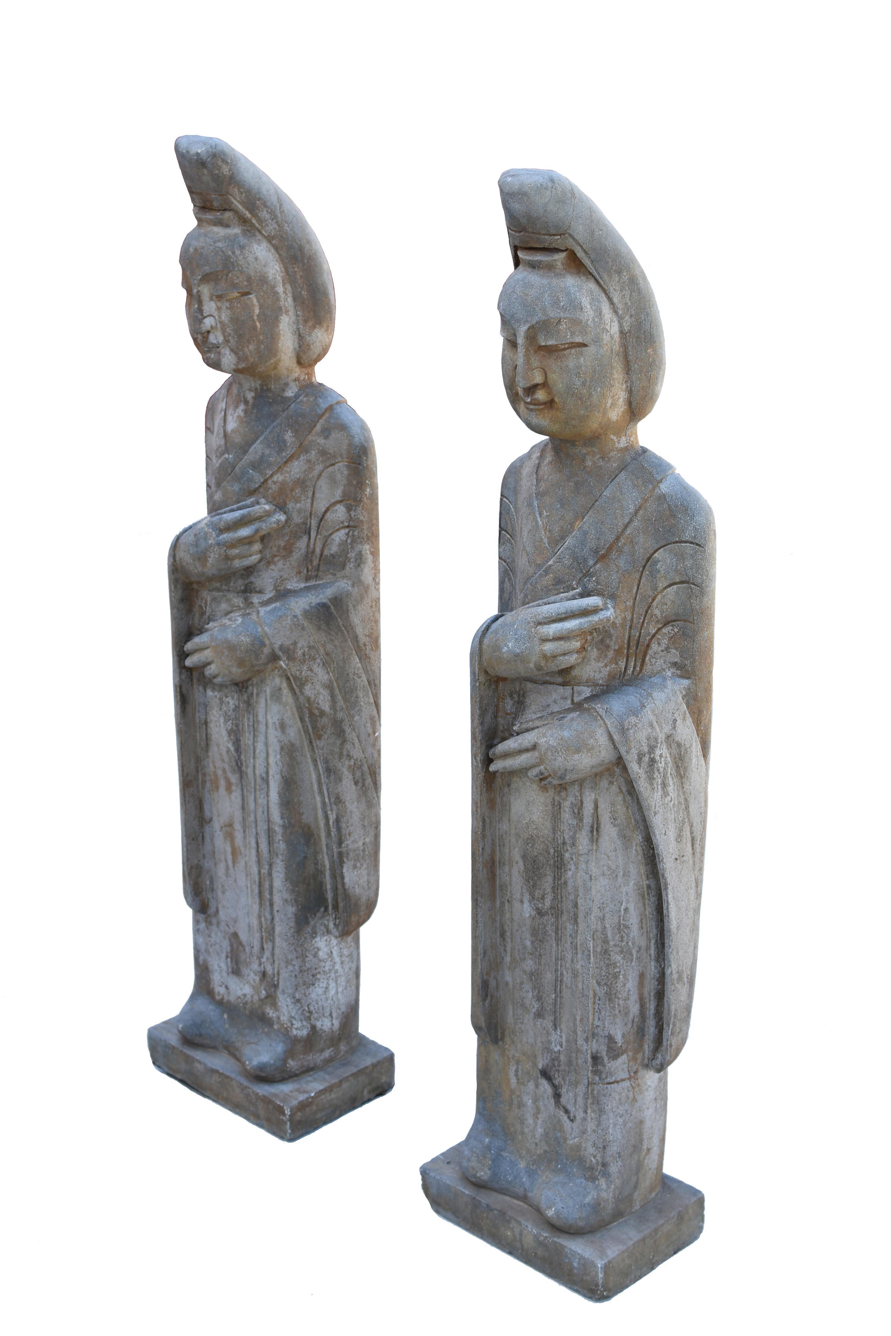 A pair of 20th century solid stone court lady statues. The full face is with long slender eyes under arched brows flanking a strong straight nose. Hair held tightly away from the face, gathered into a smooth coiffure, anchored by a wide pin above