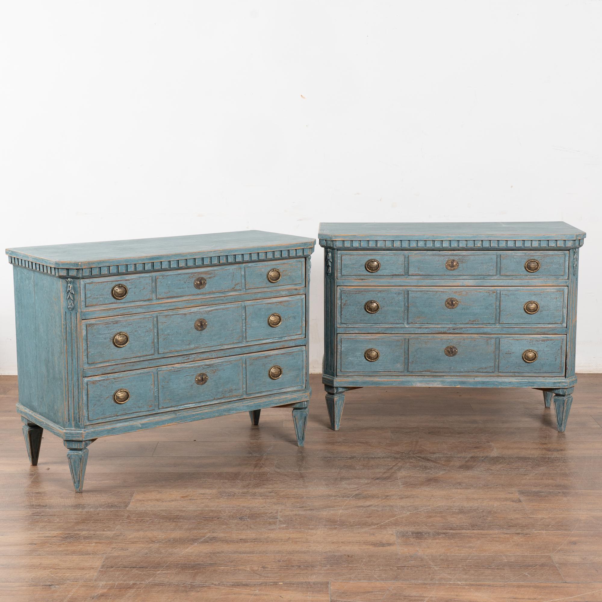 Paire d'élégantes commodes à trois tiroirs en pin de style gustavien, peintes dans de douces nuances de bleu.
Les montants latéraux cannelés sont ornés d'une guirlande florale sculptée, d'une moulure à denticules et reposent sur quatre pieds fuselés