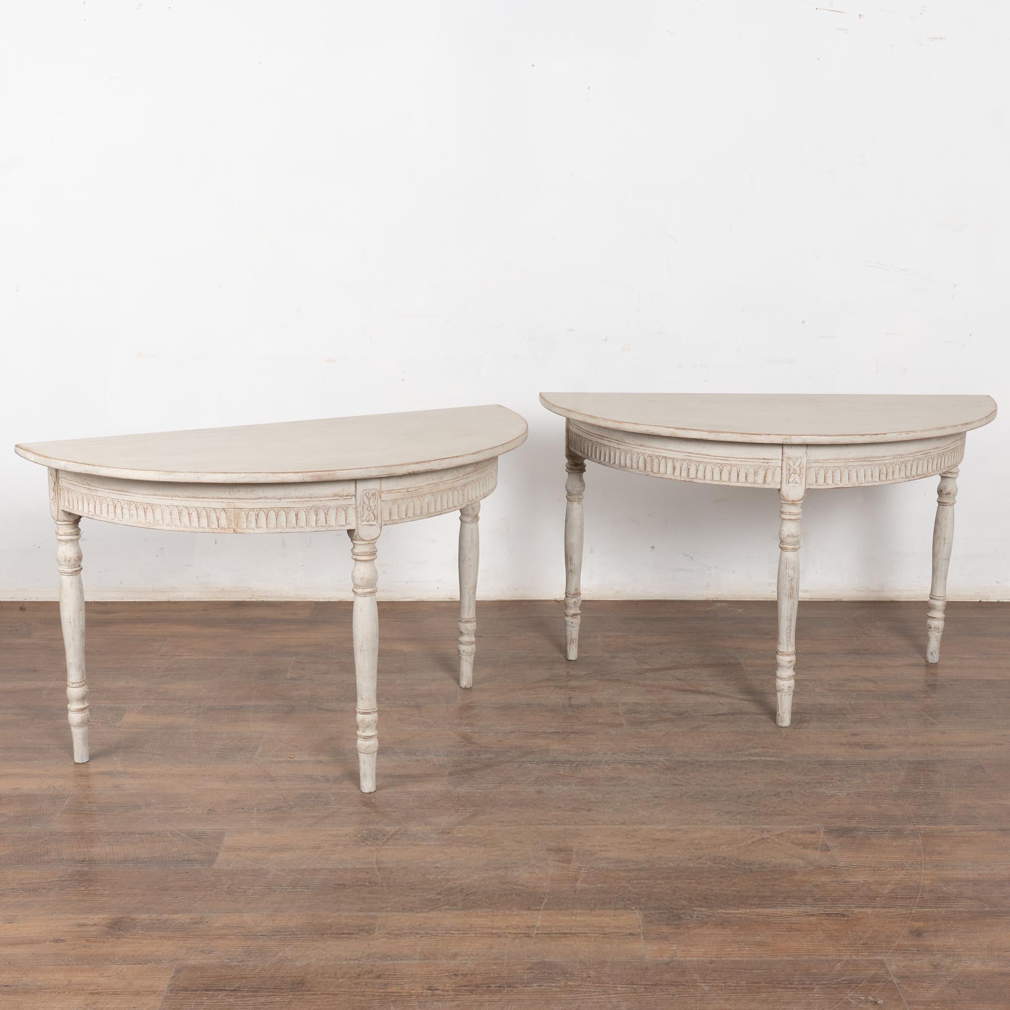 Paire de tables d'appoint ou de consoles en demi-lune de style gustavien. 
Les pieds tournés et les sculptures décoratives en forme d'œuf et de fléchette le long de la jupe ajoutent à l'attrait intemporel de ces demilunes.
Finition peinte en couches