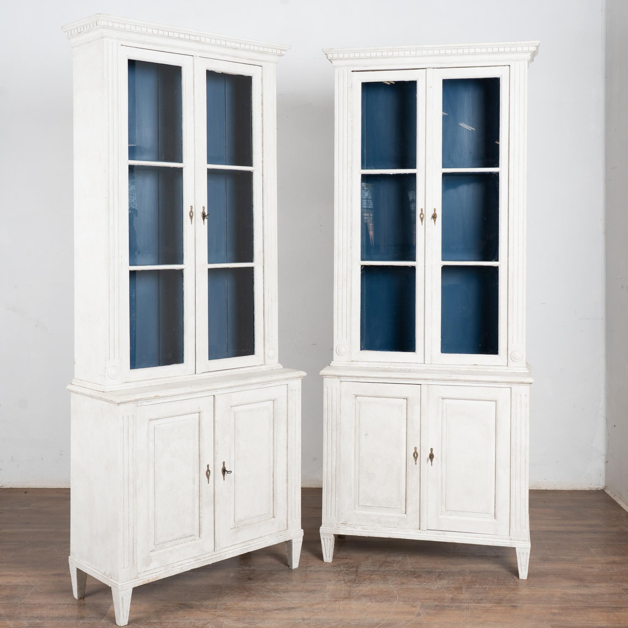Pair of tall Gustavian style white painted pine bookcases standing 7.5' tall.
Dentil molding along crown and traditional fluted tapered feet. Two interior upper shelves and one lower shelf, all adjustable with original 