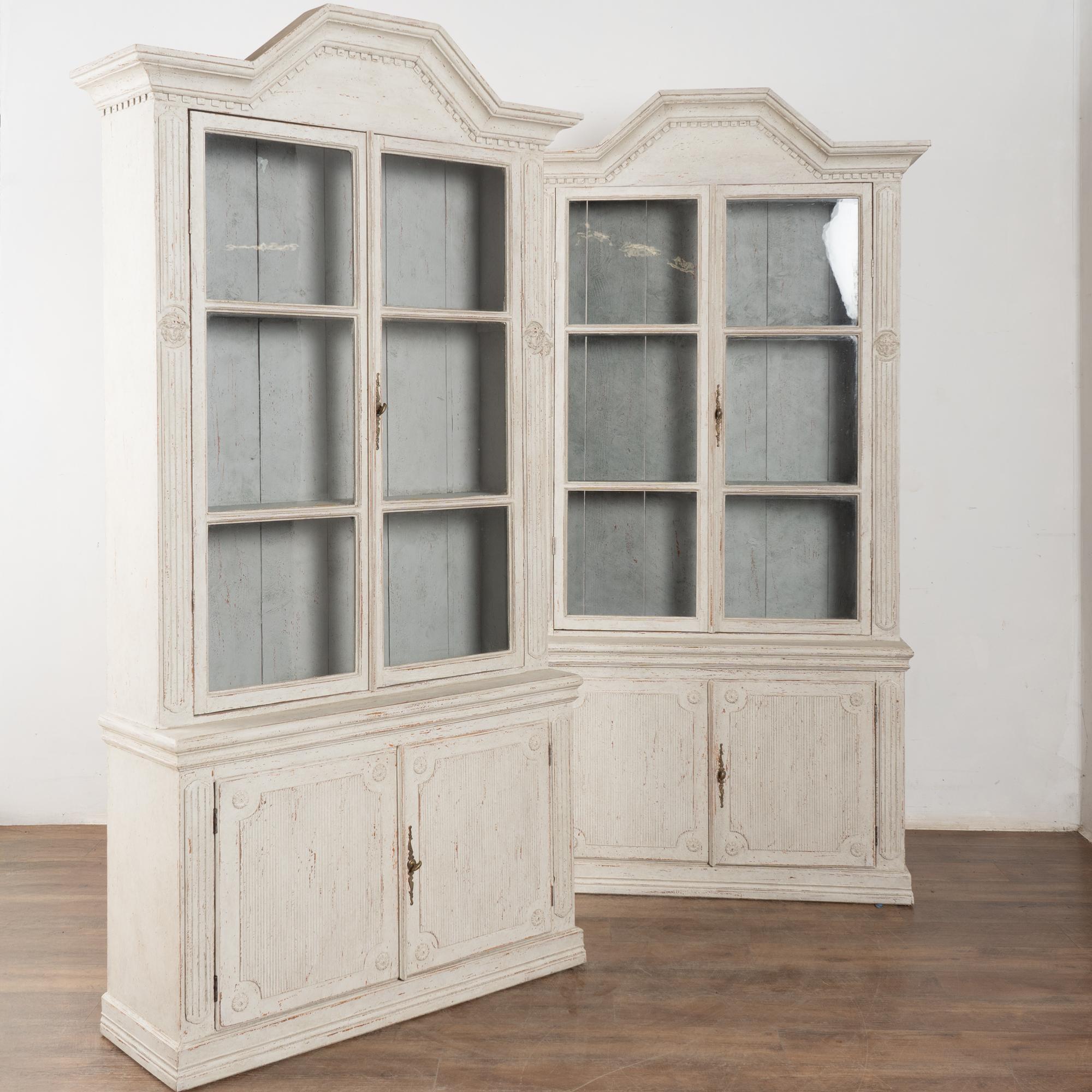 Paire de grandes bibliothèques en pin peint en blanc, de style Gustavien, mesurant un peu moins de 8 pieds de haut.
Moulure en denticule le long de la couronne et sculpture cannelée traditionnelle le long des panneaux de porte des armoires. Deux