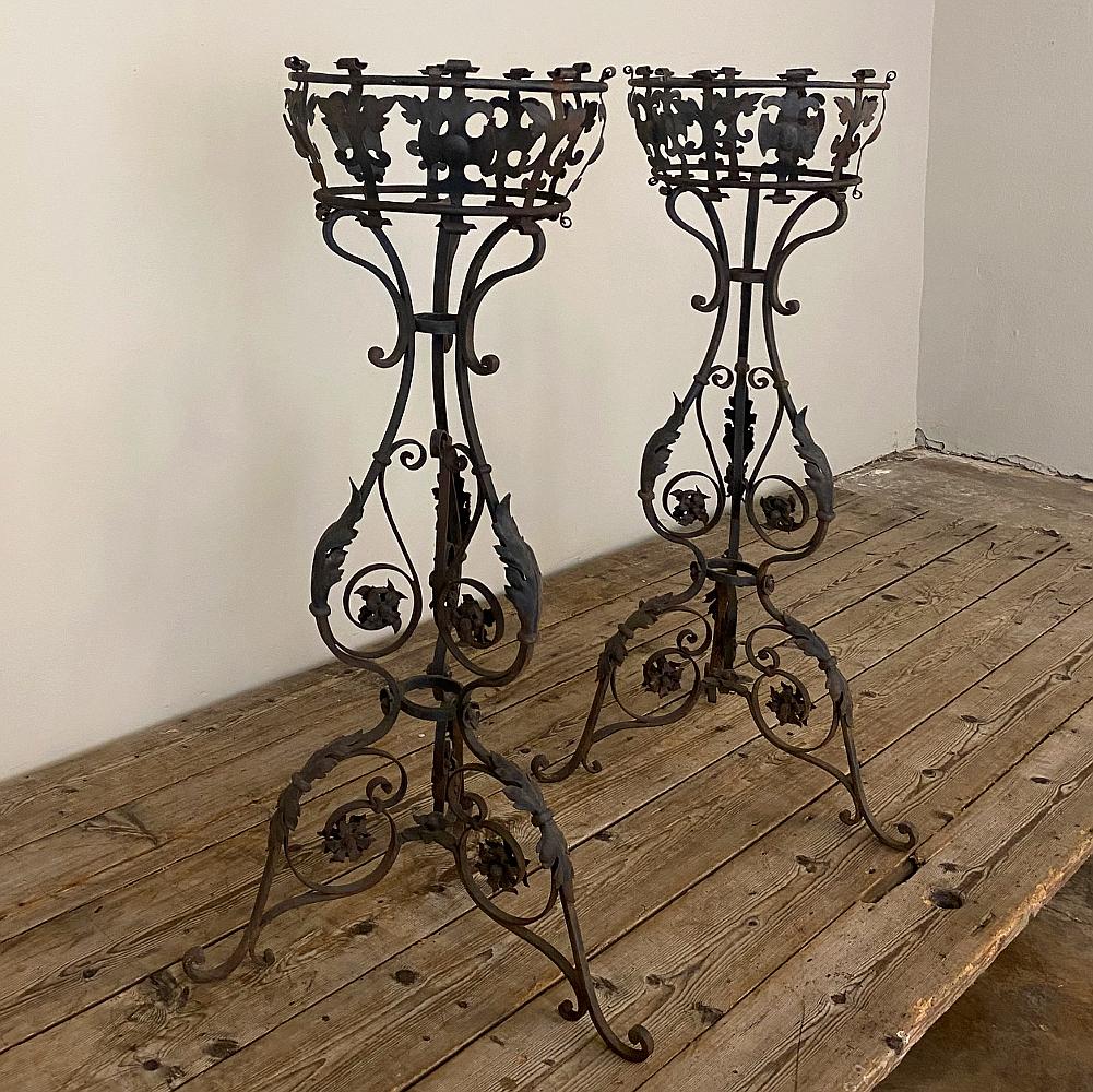 Pair 19th century wrought iron jardinières, plant stands are the perfect way to add style, flair and symmetry to your indoor or outdoor space! The graceful shape of the design includes a basket with ivy leaf and Fleur de Lys on top, supported by