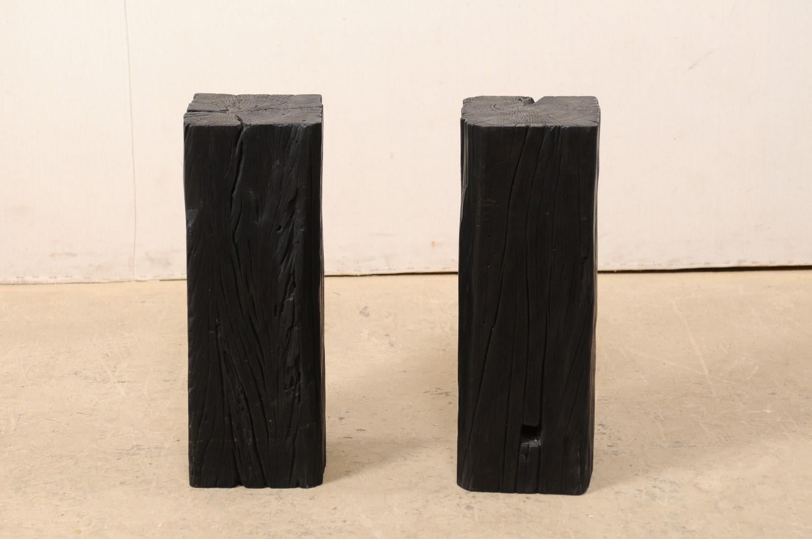 A pair of carbonized wood columns. This pair of unique pedestals, with squared bodies, have been created from old, reclaimed Merbau wood which has been carbonized, giving it a wonderful rich, black patina. The tops are primarily smooth and flat,