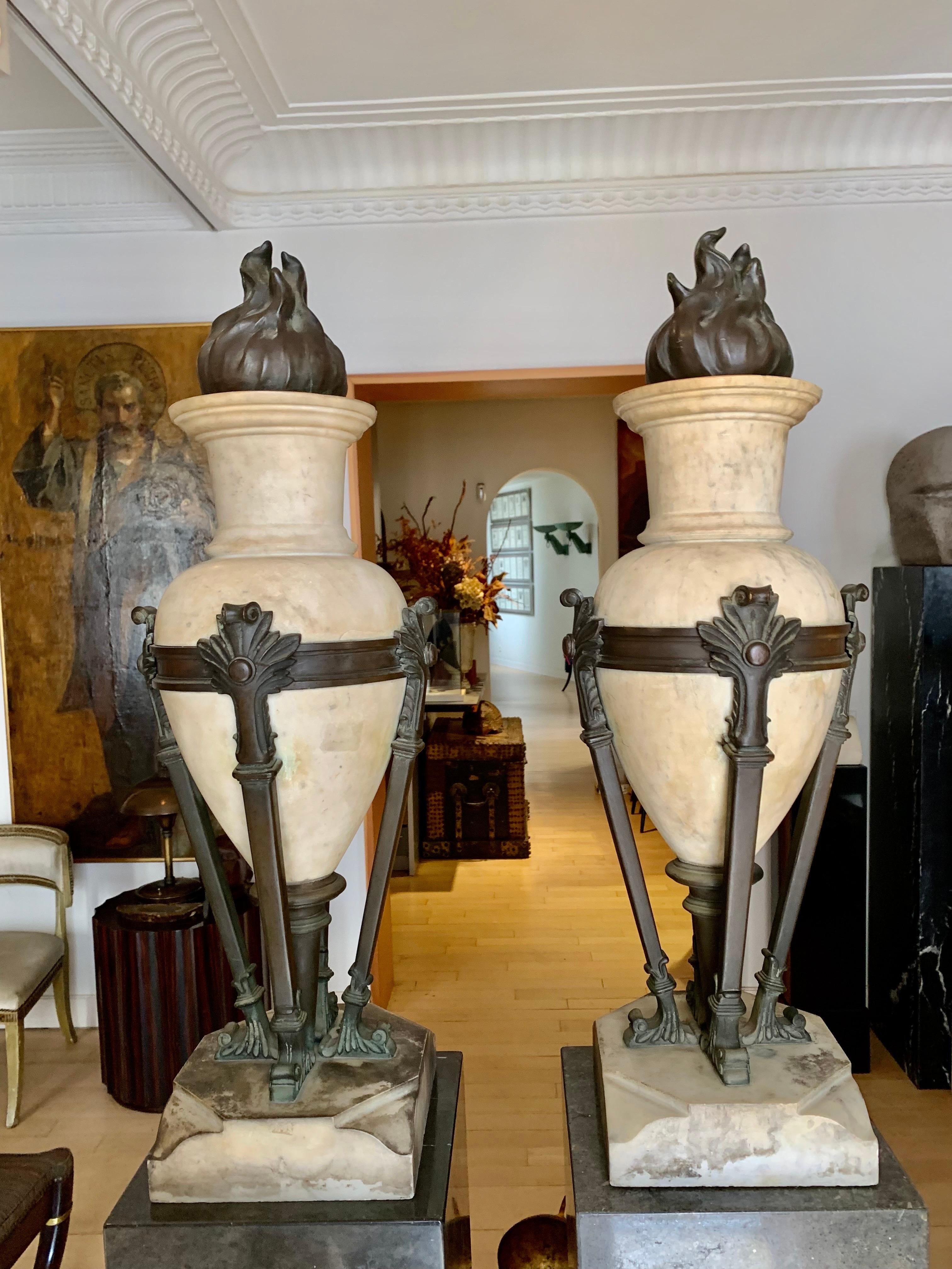 A pair of impressive and large vases or urns from the Art Deco period, made of white marble and patinated bronze, the cups in the shape of an amphora or Greco-Roman vessel, are supported by a circular bronze structure, from which four legs emerge on
