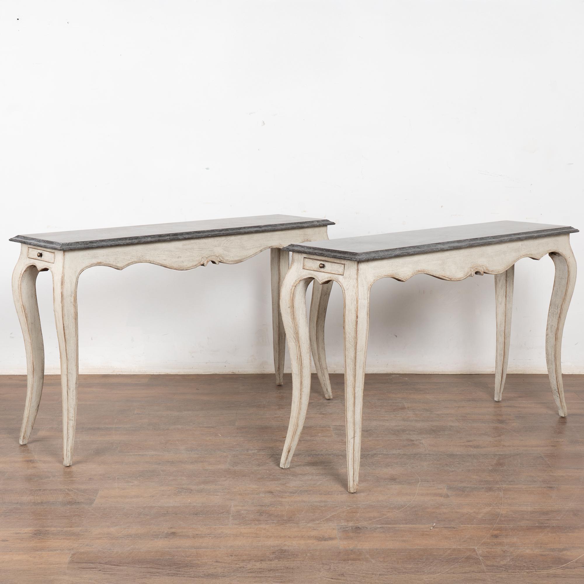 Early 20th-century pair of Swedish oak console tables with newer professionally applied white painted finish, distressed to complement their age and form.
ach features a beveled marble top in tones of steel gray and plum undertones, with long
