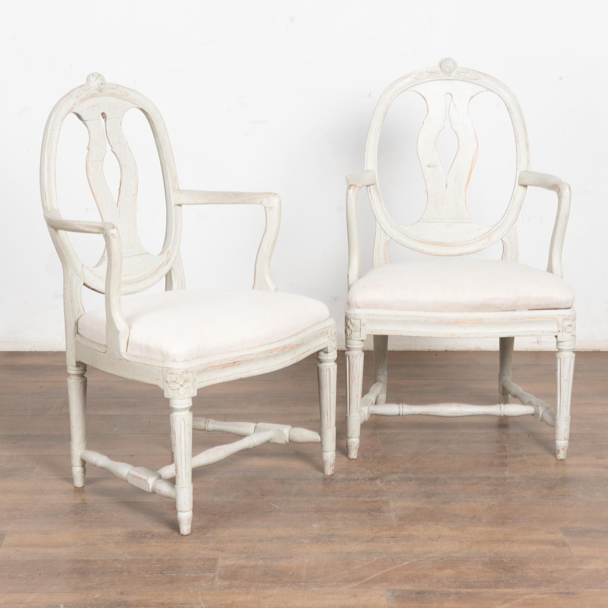 Pair, attractive Swedish country Gustavian style painted arm chairs with distinctive round back topped by carved rosettes.
Turned, fluted legs and carved accents along the skirt add to the graceful charm of this pair.
The newer, pale gray/antique
