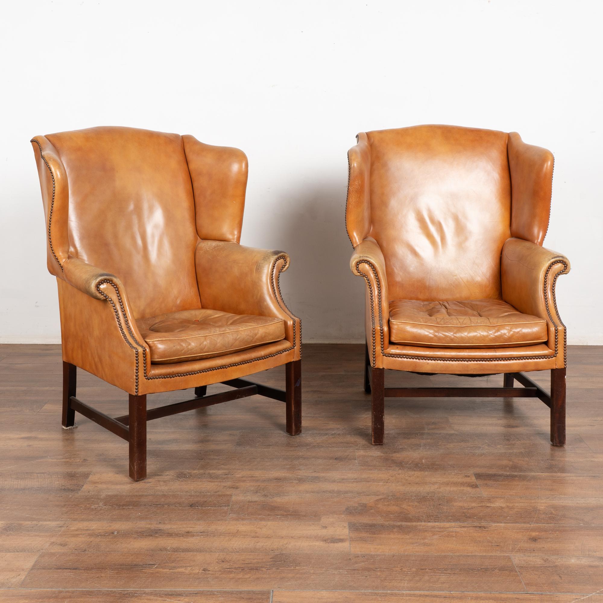 Vintage brown leather wingback arm chairs with classic nailhead trim.
Sold in vintage used condition. Frame is solid/stable and sits low. Seat buttons are a contrasting color to the seat leather. 
Leather shows signs of use and wear including