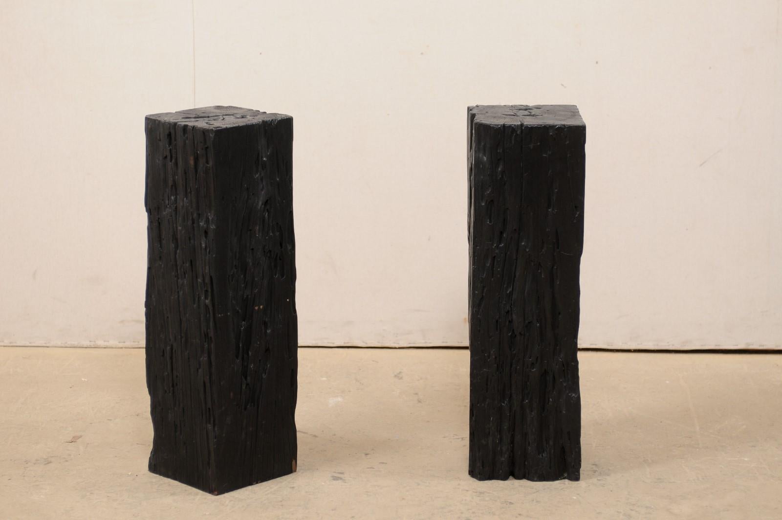 Une paire de colonnes en bois carbonisé. Cette paire de piédestaux uniques, aux corps carrés, a été créée à partir de vieux bois Merbau récupéré qui a été carbonisé, ce qui lui donne une magnifique patine noire et riche. Les dessus sont