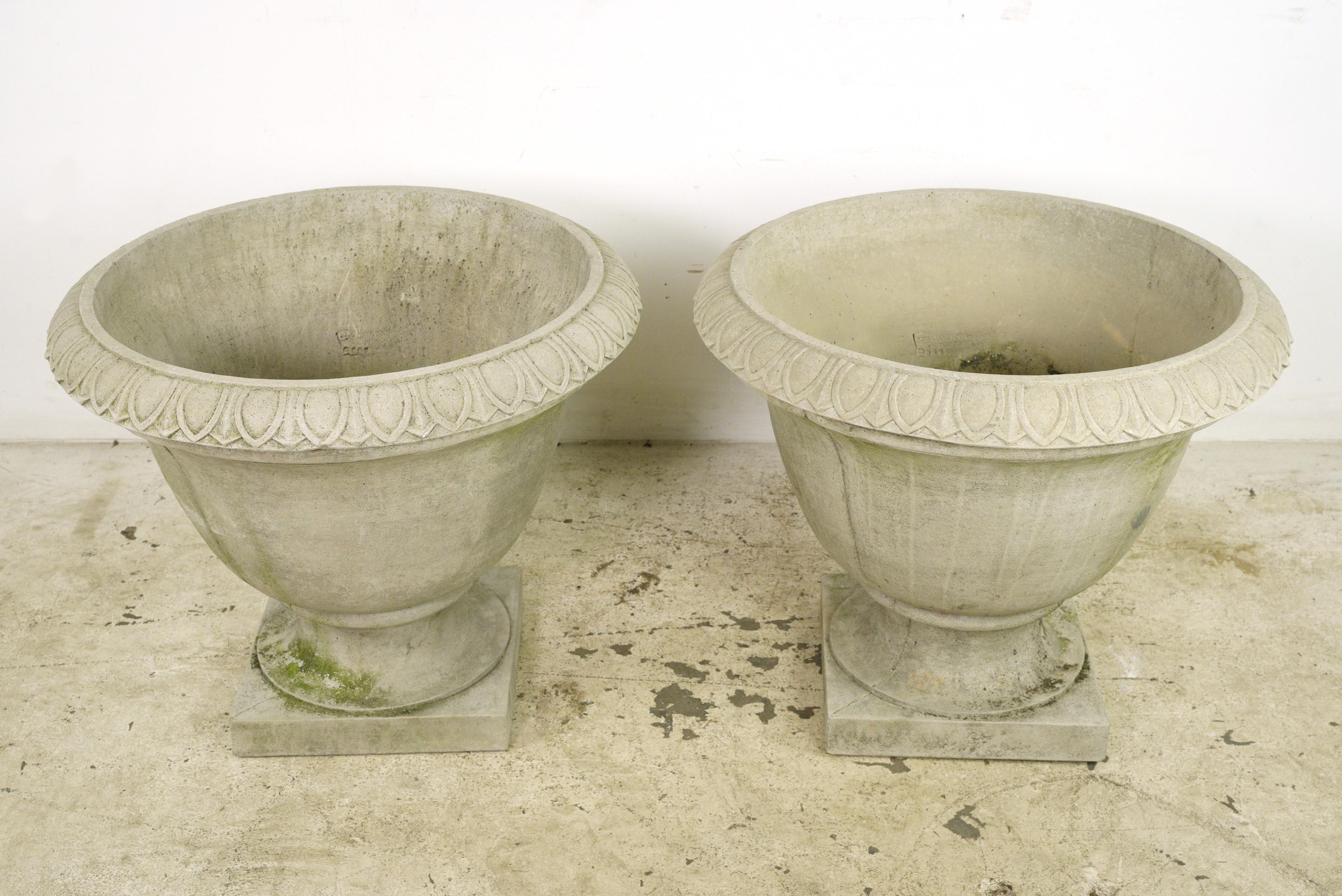 This pair was procured from an esteemed estate located in Greenwich, Connecticut. These urn-shaped planters feature distinctive egg and dart trim detailing. Crafted from durable concrete, they provide a sturdy foundation for planting. They are in