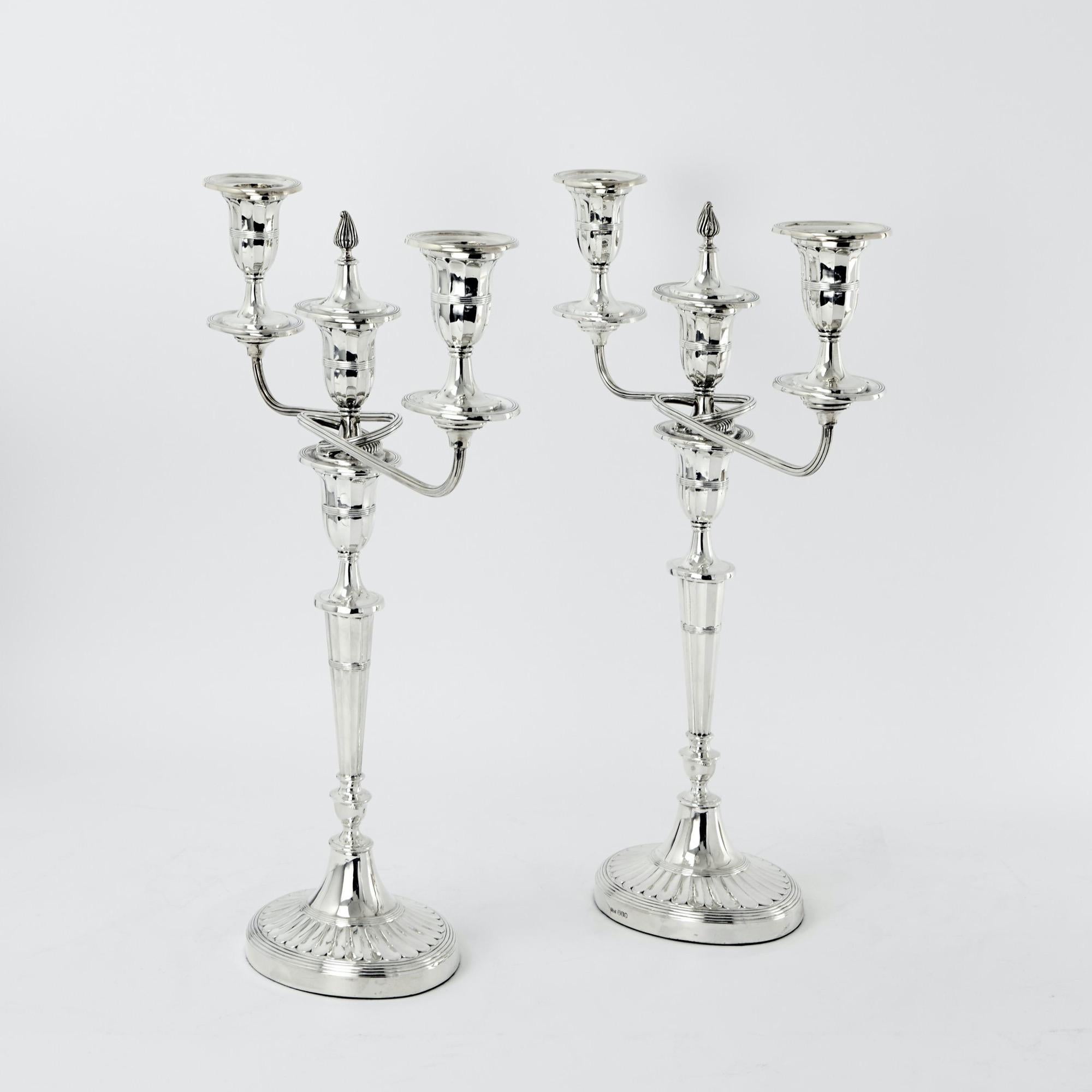 Coppia di candelabri ovali a tre luci in argento sterling nello stile George III, che era originariamente popolare alla fine del XVIII secolo. I candelieri sono elegantemente scanalati alla maniera georgiana, ciascuno con una fiamma o uno snuffer