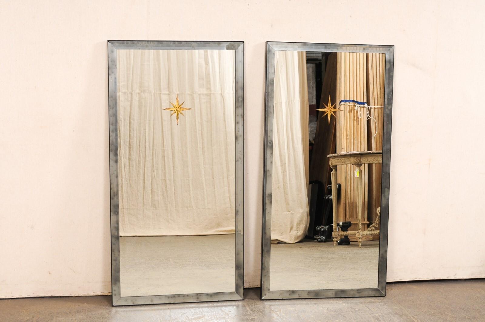 A pair of Artisan made mirrors with gold églomisé sunbursts and antiqued mirrored glass surround. This pair of rectangular-shaped mirrors stand just over 4 feet in height. They are artisan made and have a clear mirrored center, framed within a