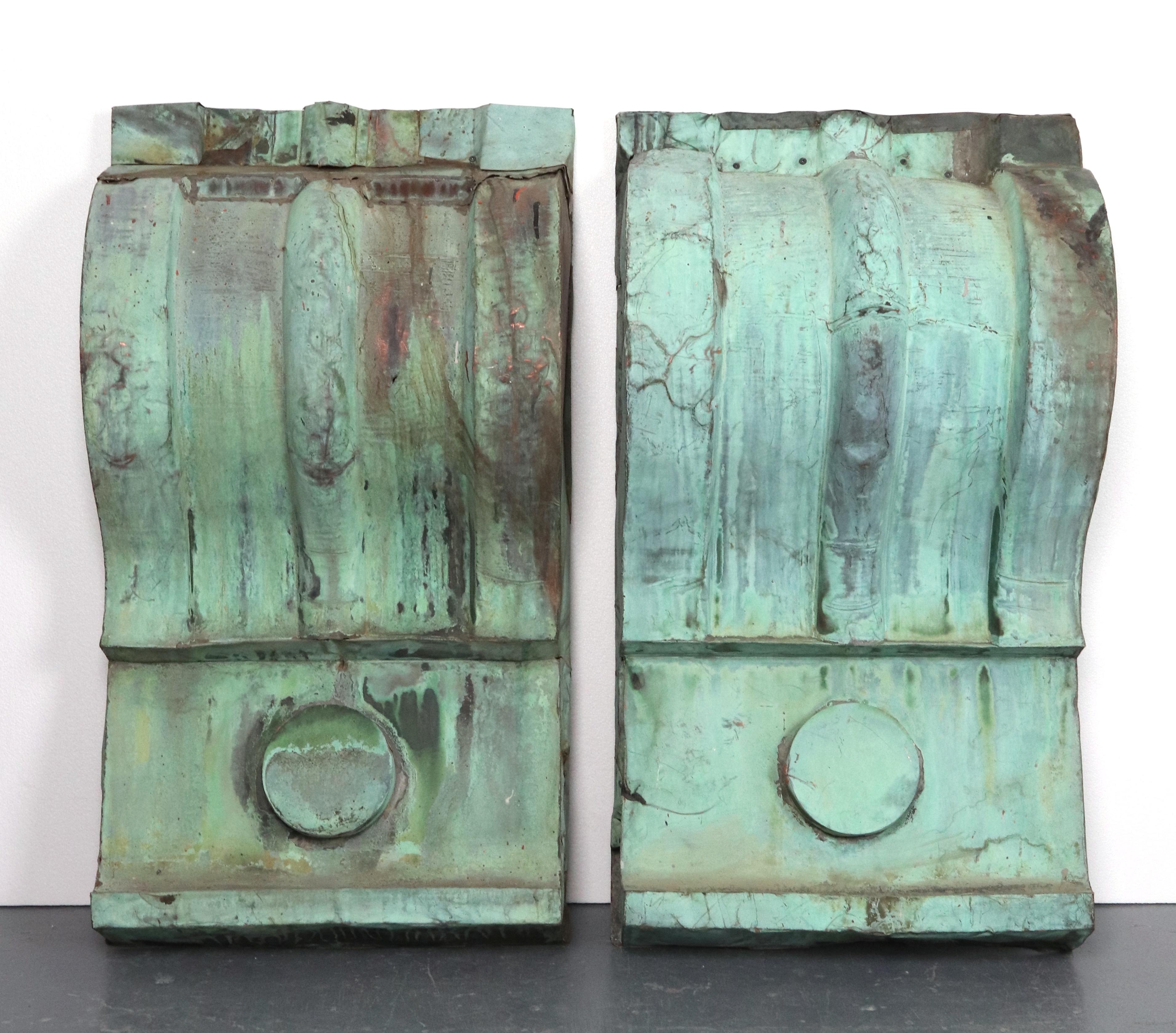 Reclaimed antique copper corbels with a curved design and a circular element at the base. The surfaces show signs of weathering, including cracks and discoloration. We installed a wood backing for ease in wall mounting. Priced as a pair. Please