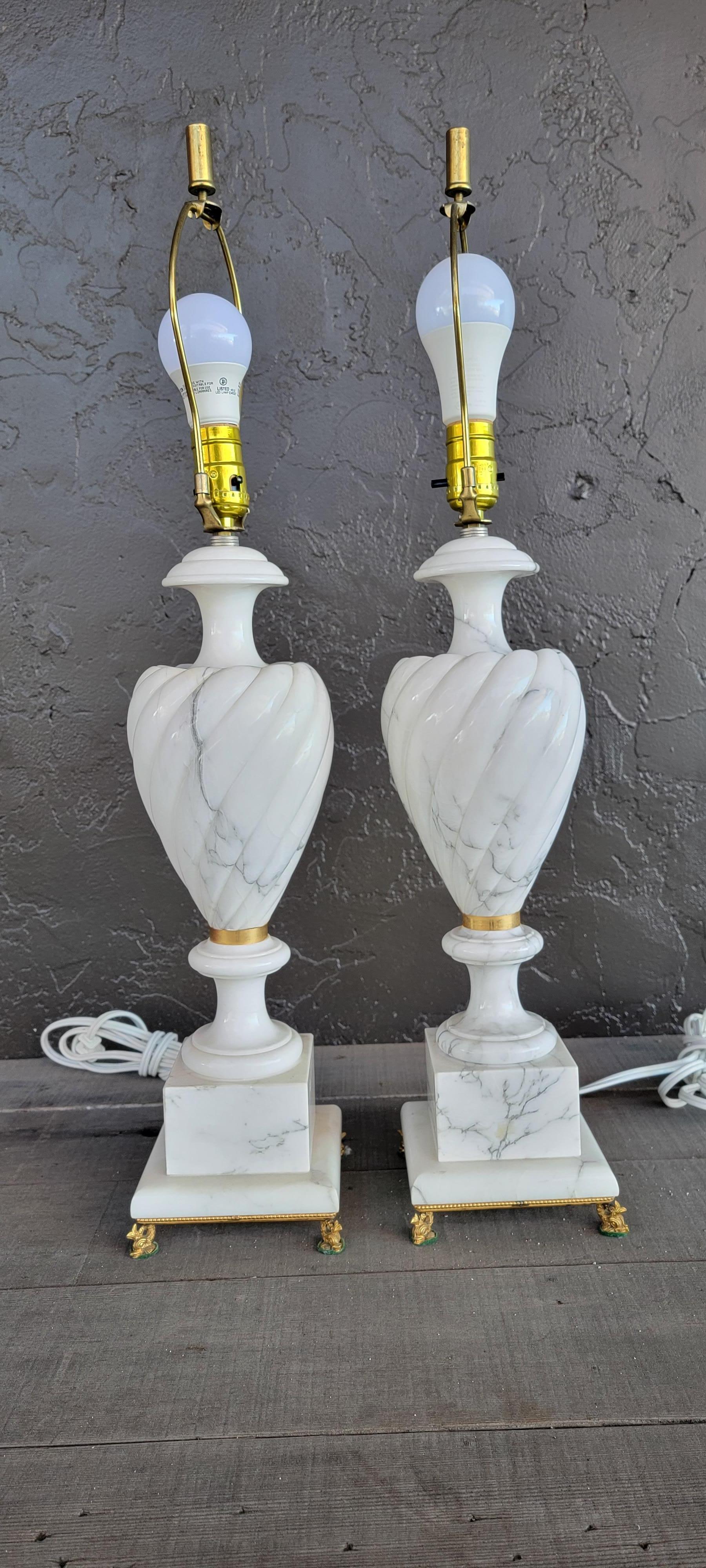 A pair of alabaster table lamps mounted to gilt brass dolphin bases. Black and white marbleized alabaster. Measure 28.25 inches to top of finial. Base measures 5.5 inches square.