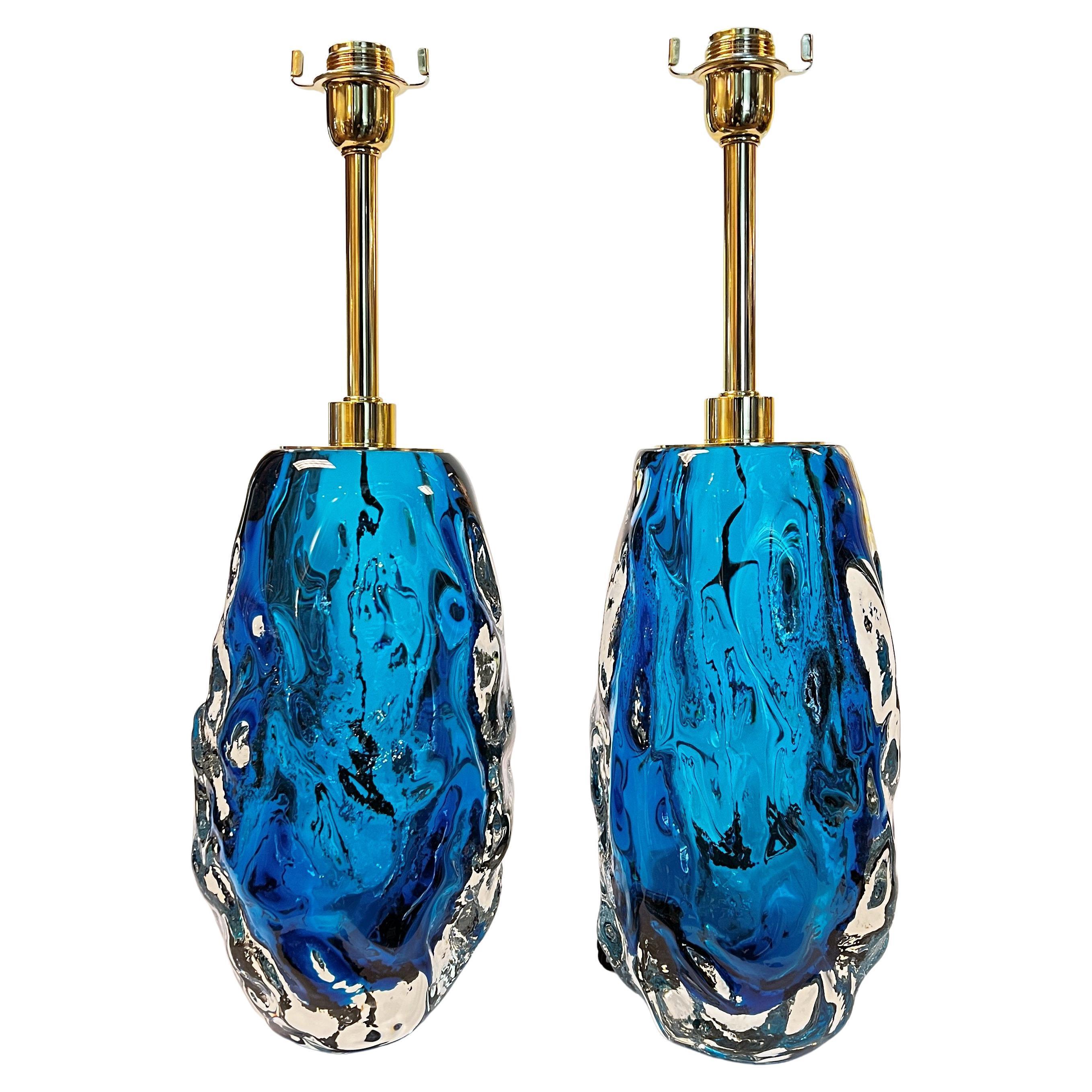 Our pair of table lamps by Alberto Dona (Italian, 1944- ) are crafted from brilliant shimmering blue and clear glass in undulating ovoid shape with polished, lacquered brass hardware. With American sockets and wiring. 23.5 in tall and the glass