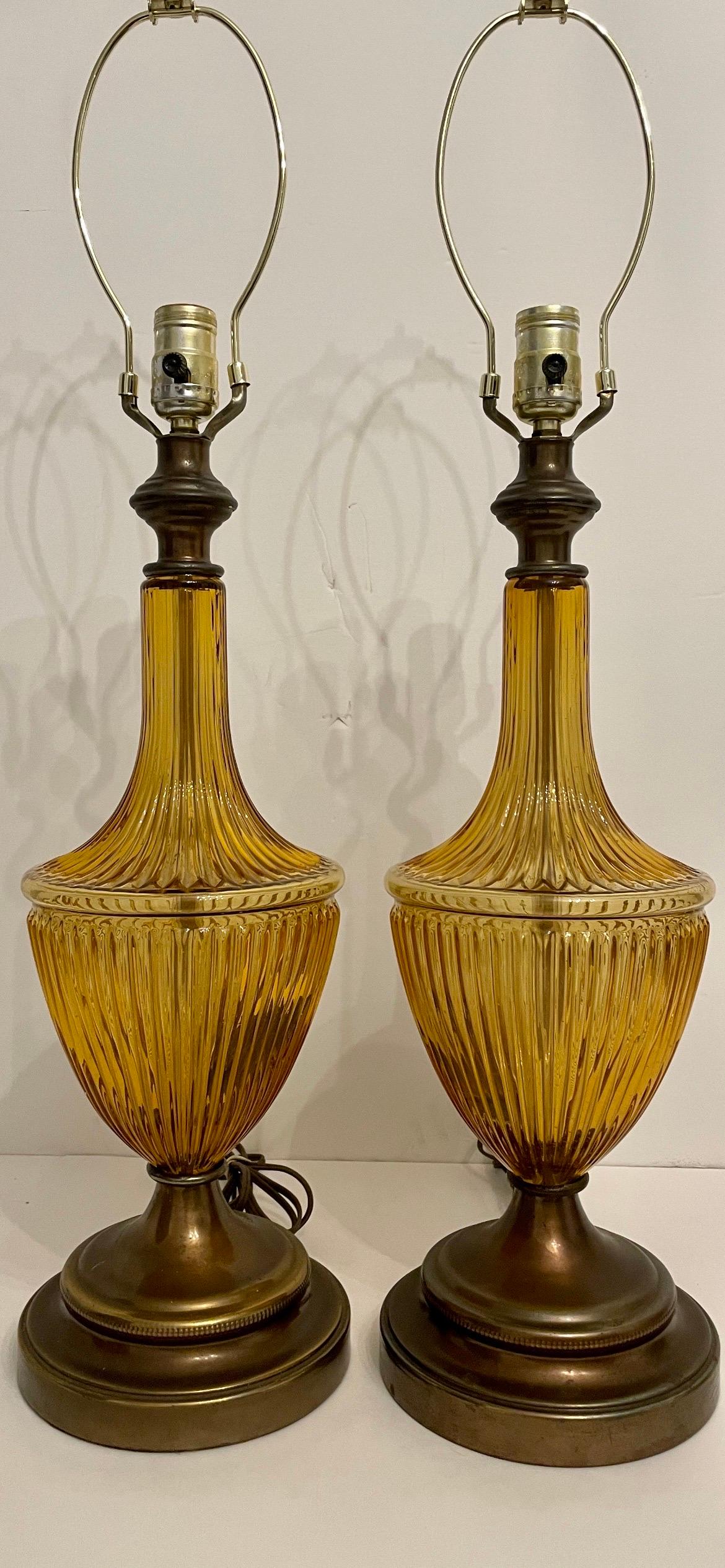 Pair Mid Century Amber glass lamps. Urn form ribbed amber glass with antique brass base and fittings. Any dark spots in glass is reflection or shadow. Bases have slight patina spots. 7