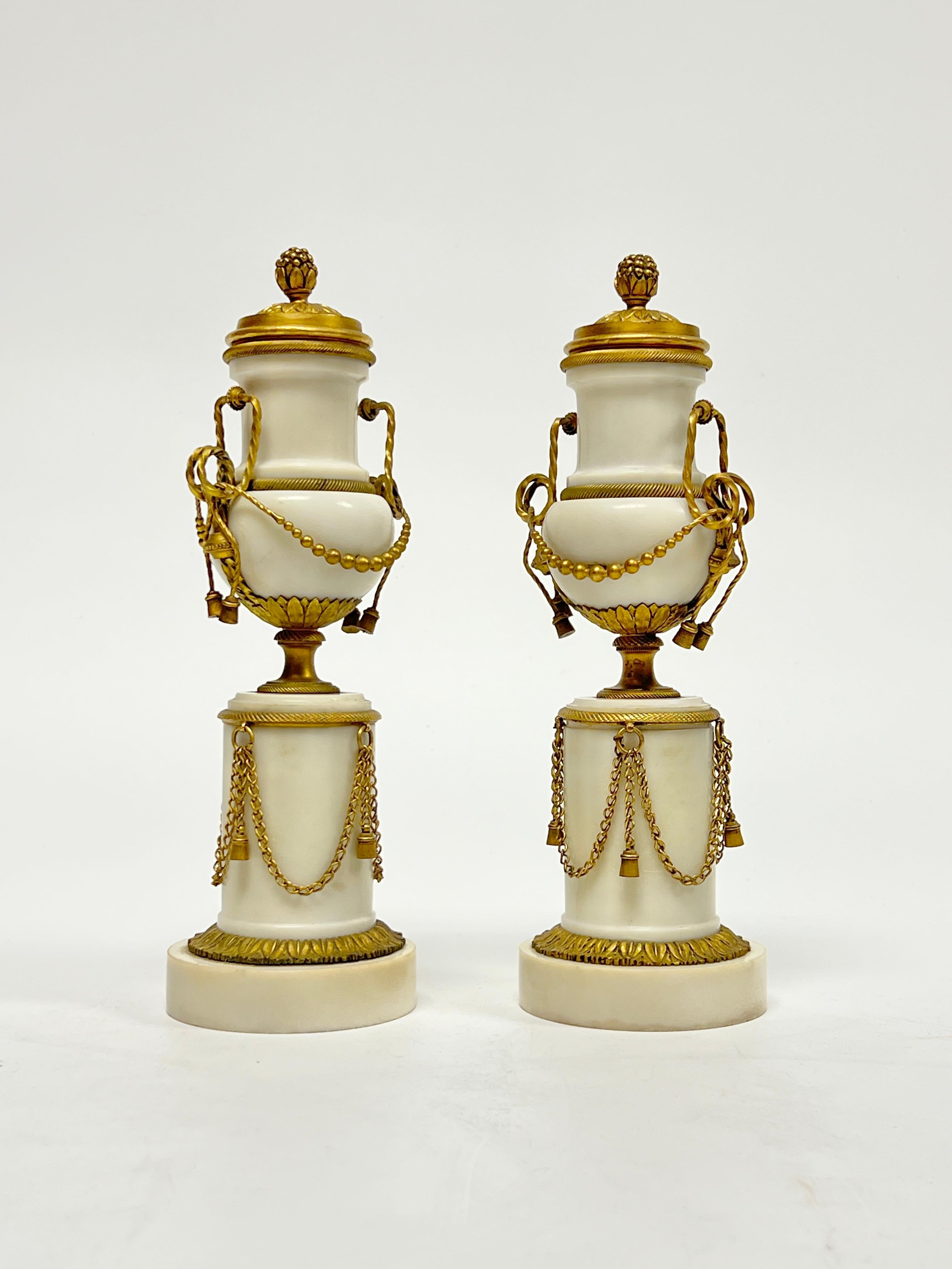Pair of antique (19th century) candle holders in the French Louis XVI style, crafted from white marble with gilt bronze standards and mounts including draped bronze chains and covers.  Each 9 1/2 by 3 by 3 inches.