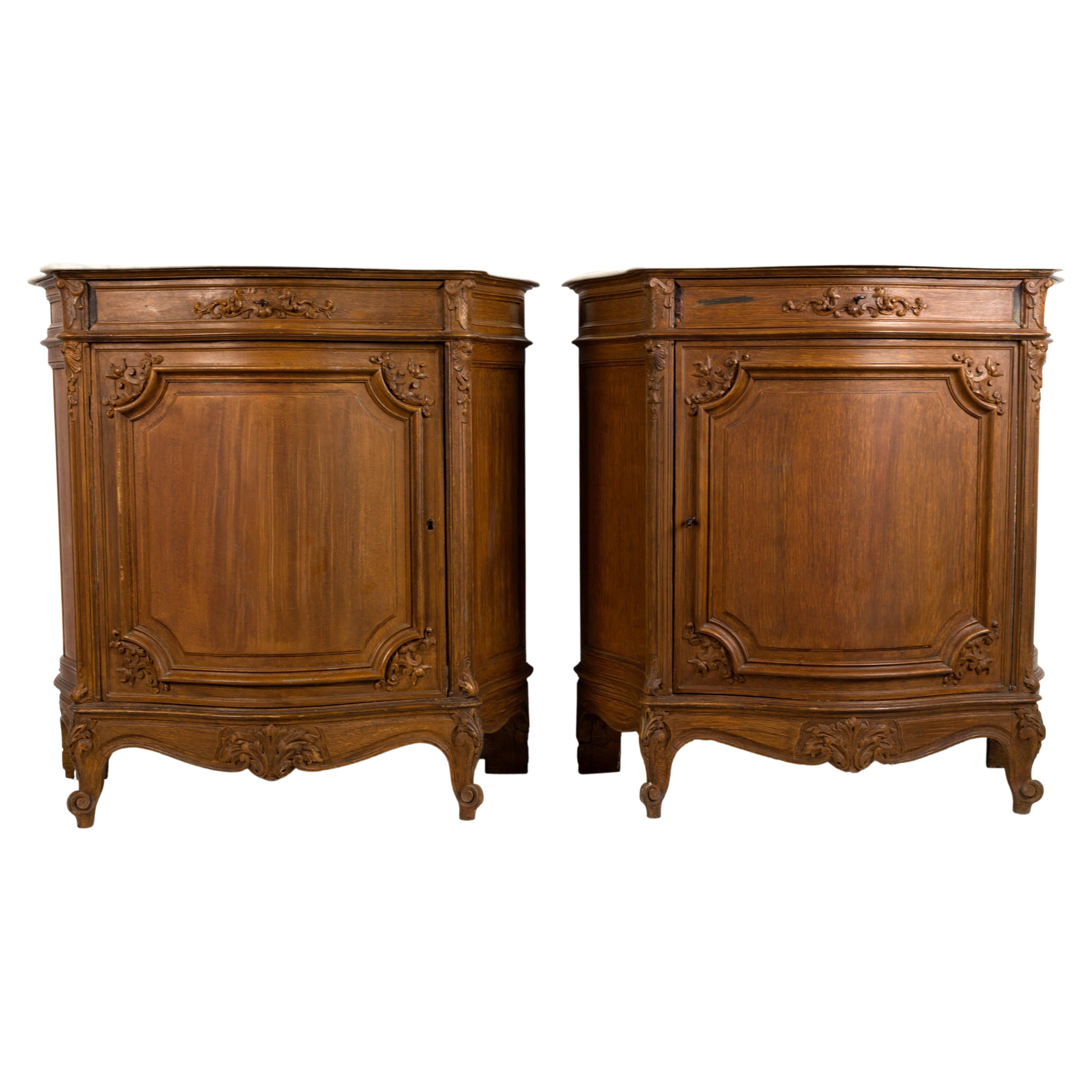 A pair of 19th century French serpentine commodes in the Louis XV manner.
Each with a marble top above a frieze of one short drawer above a central door, the surfaces with scrub painted panelling and carved detailing, all terminating in escargot