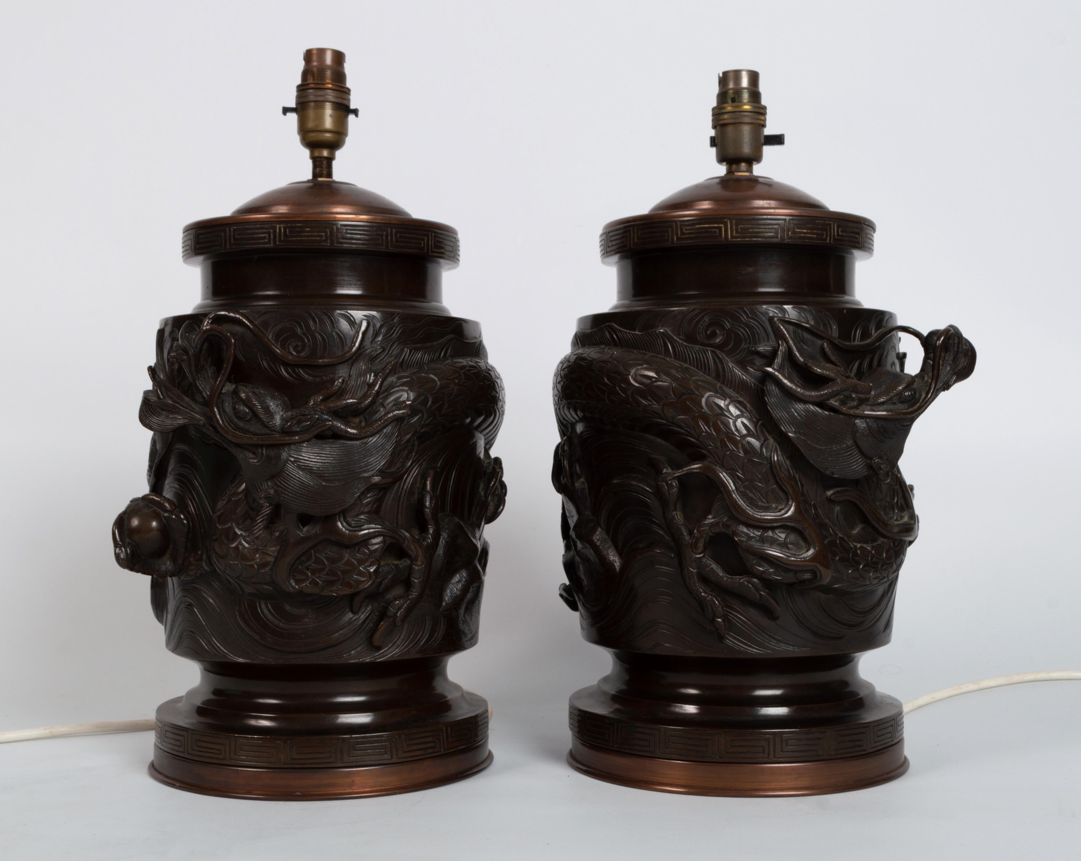 A pair of antique 19th century Meiji Period Japanese patinated bronze vase table lamps.

A pair of Japanese patinated bronze vases of cylindrical form, cast with mythological creatures amongst prunus, Greek key pattern to rim and foot. Fitted for