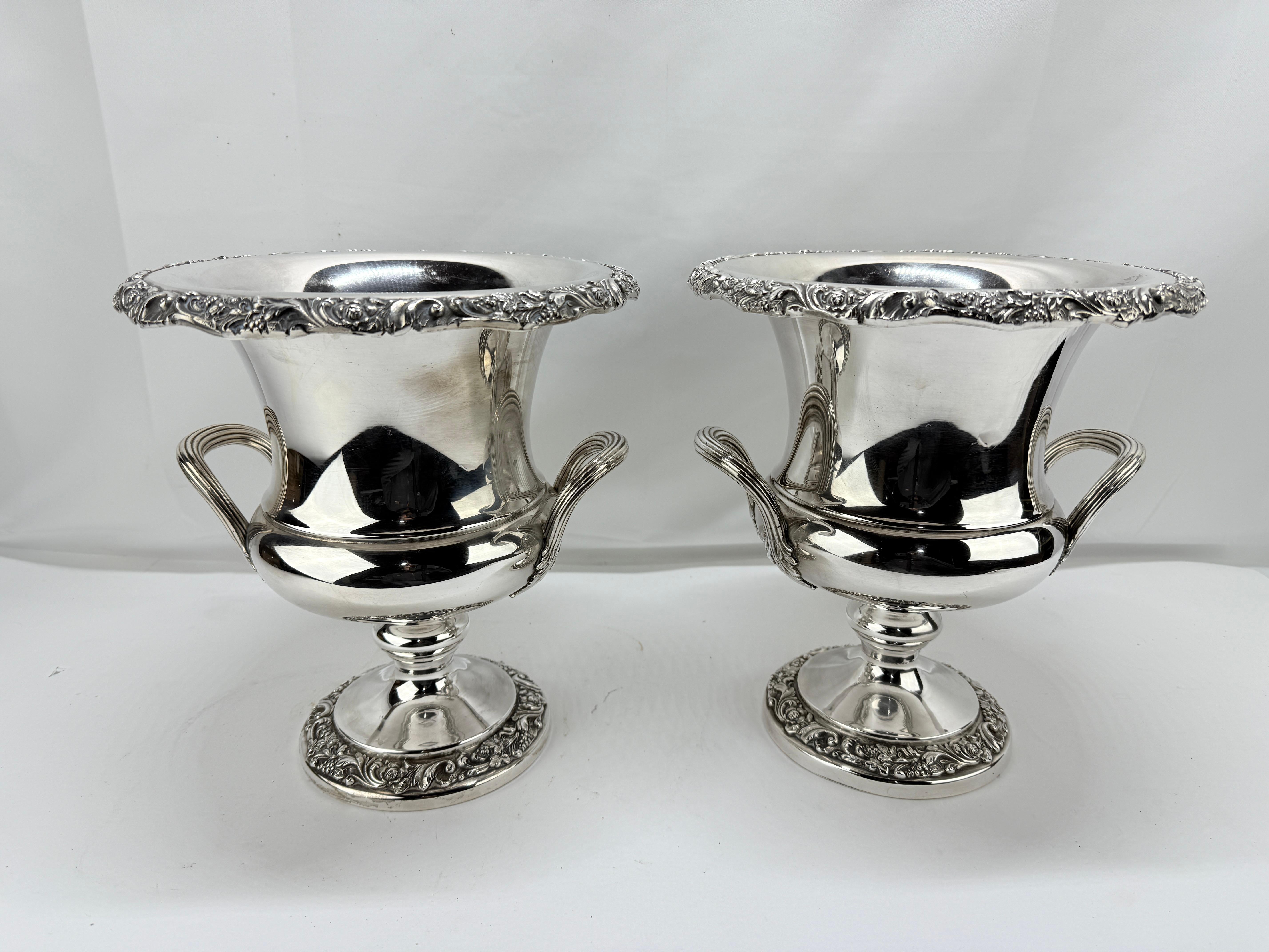 This elegant pair of silverplate trophy form champagne coolers, produced by Webster Wilcox, embodies timeless sophistication and refined craftsmanship. Measuring 11.125 inches in height and 10 inches in width, these coolers showcase a classical