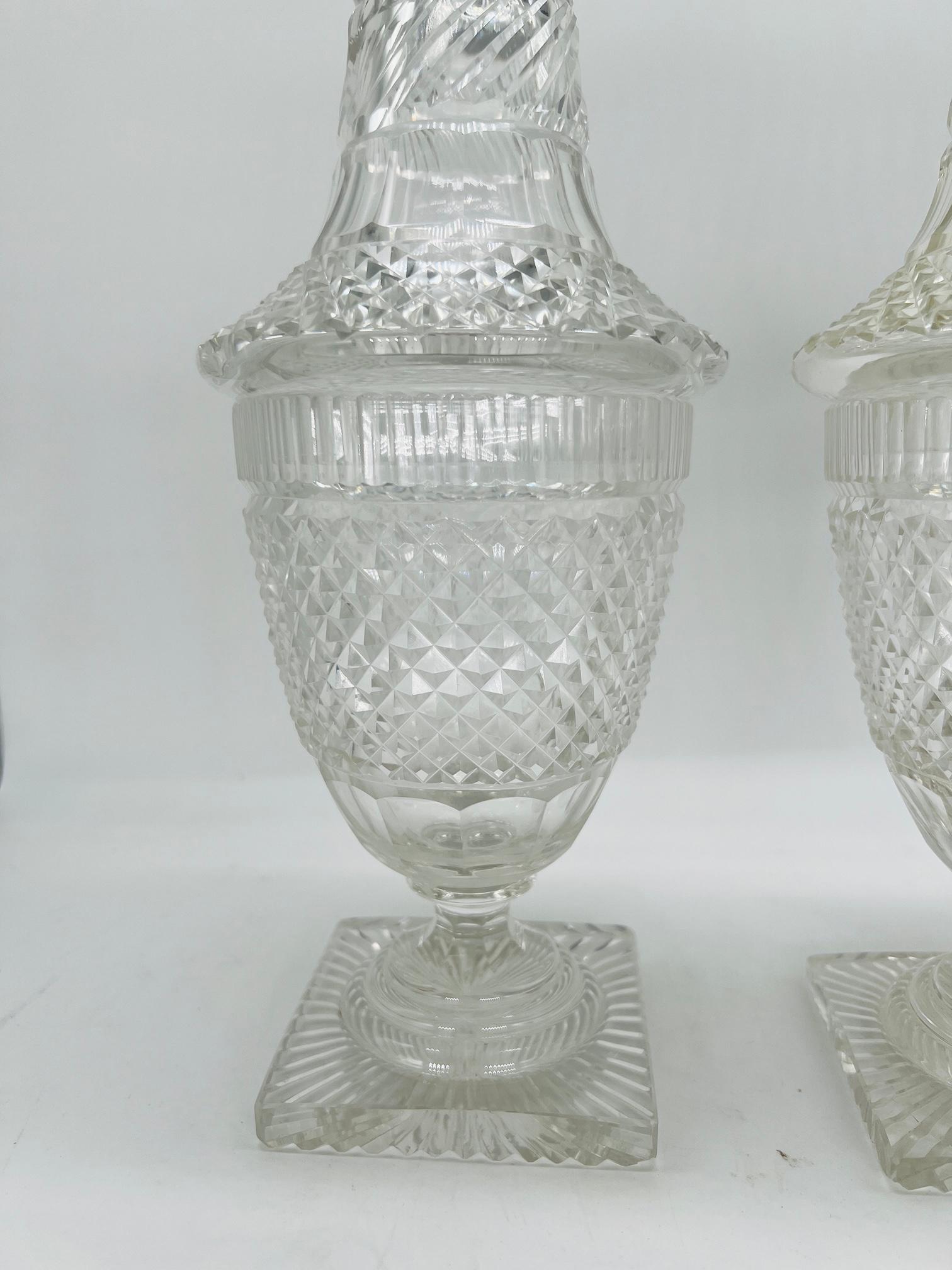 Cette élégante paire de jarres à couvercle en verre taillé anglo-irlandais témoigne du raffinement de l'artisanat de la fin du XVIIIe siècle et du début du XIXe siècle. D'une taille impressionnante de 12,125 pouces, chaque pot présente des détails