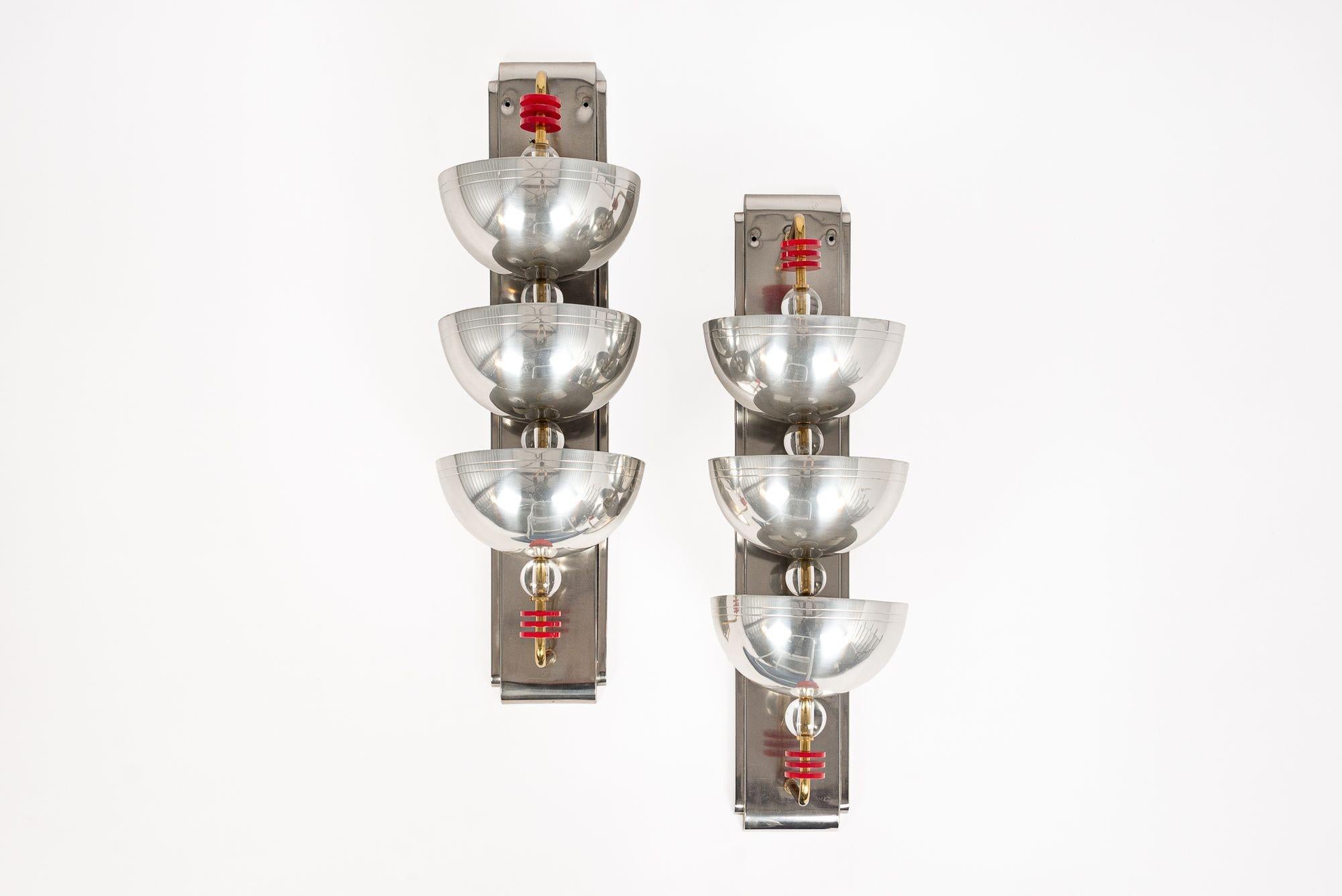 This incredible pair of antique Art Deco silver wall sconce lights are circa 1940. The sconce lamps feature three large metal cups on brass bars mounted to heavy solid metal wall plates with round, clear balls below each cup and red, disk-shaped