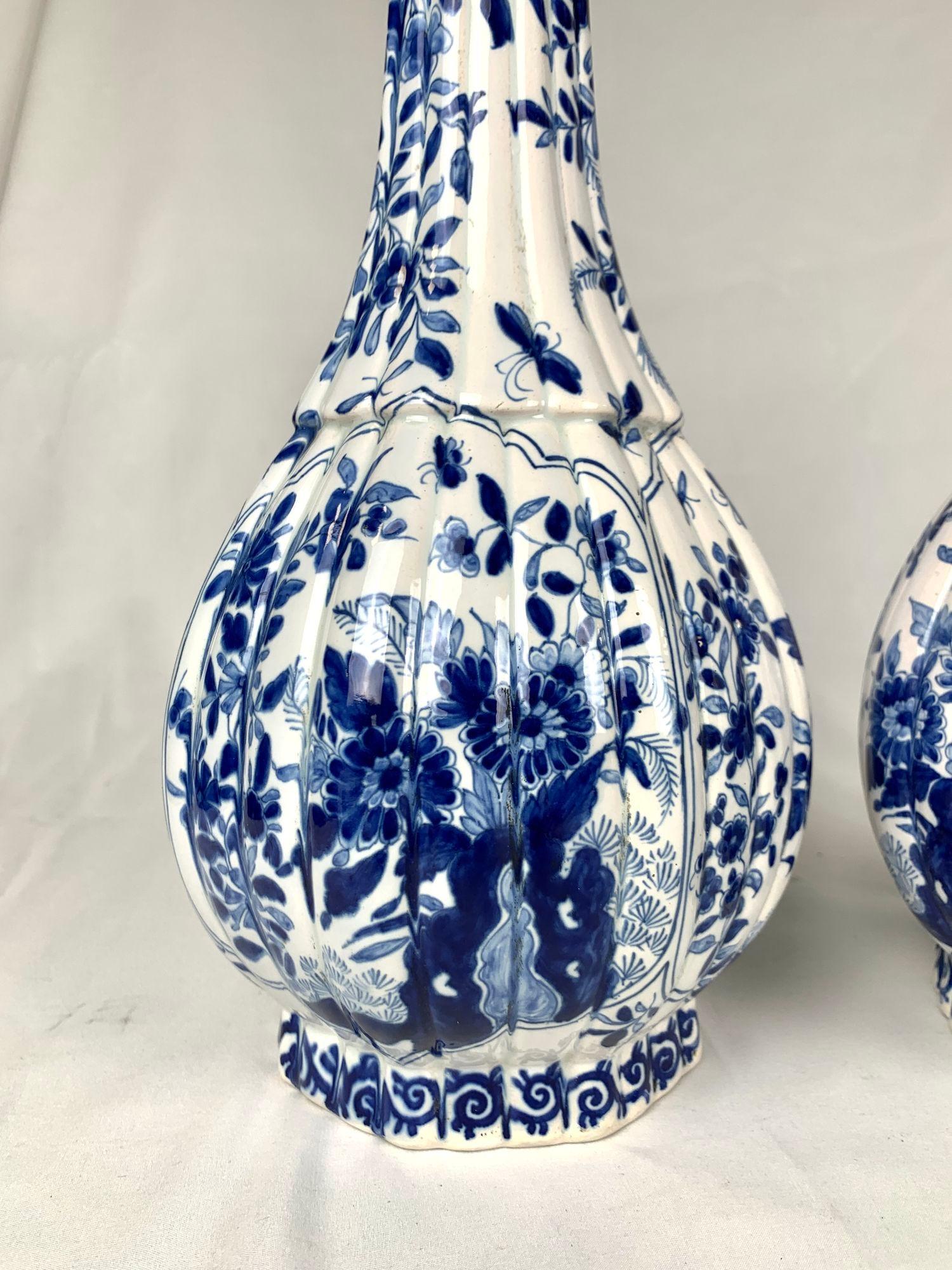 Questa coppia di alti vasi Delft blu e bianchi è stata dipinta a mano nei Paesi Bassi alla fine del XIX secolo, intorno al 1880-1890. Hanno una caratteristica silhouette a bottiglia, nota come flesvormige vaas, con un collo stretto e un corpo più
