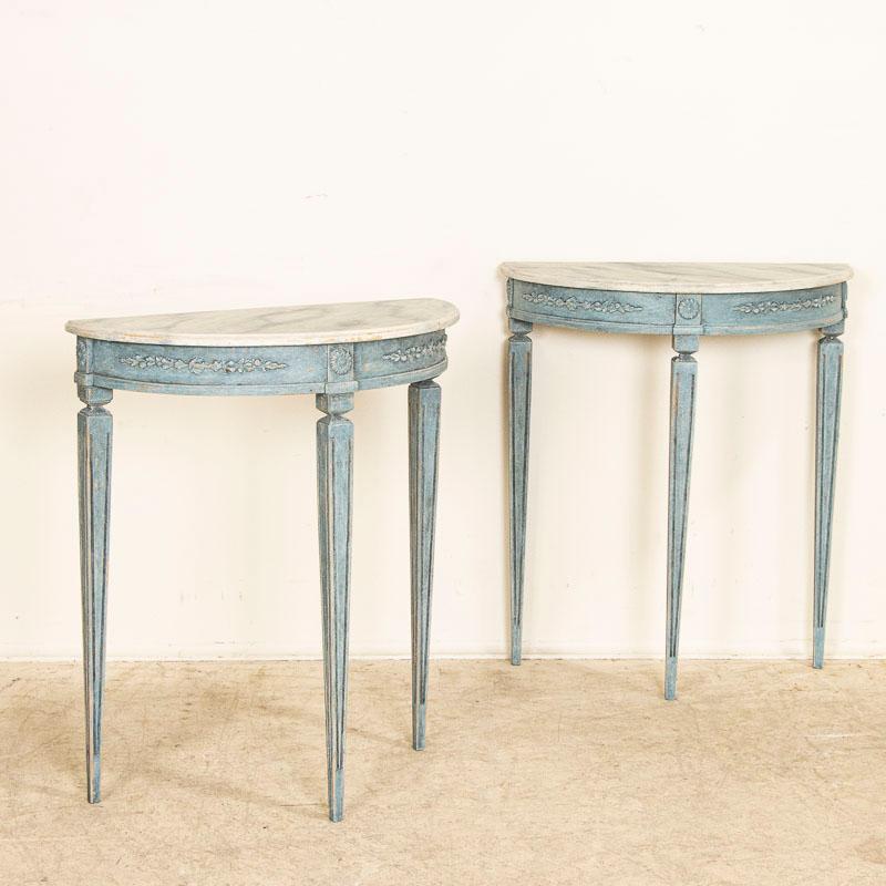 This enchanting pair of antique demi lune tables are from Sweden. Note the slender tapered/fluted legs and lovely skirt with applied carving. Both these side tables are finished with a newer, professionally applied layered blue paint and faux marble