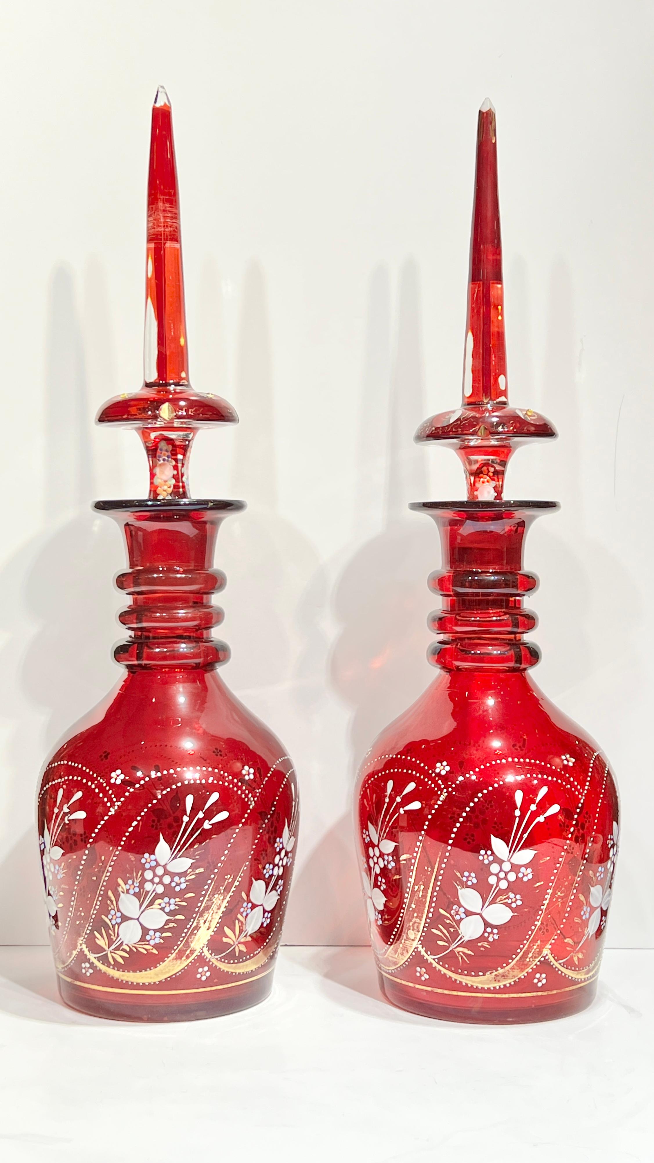 Pareja de antiguos decantadores de cristal rojo de Bohemia con adornos florales dorados y enjoyados, cada uno de aproximadamente 22 pulgadas de alto y 5 3/4 pulgadas de ancho.