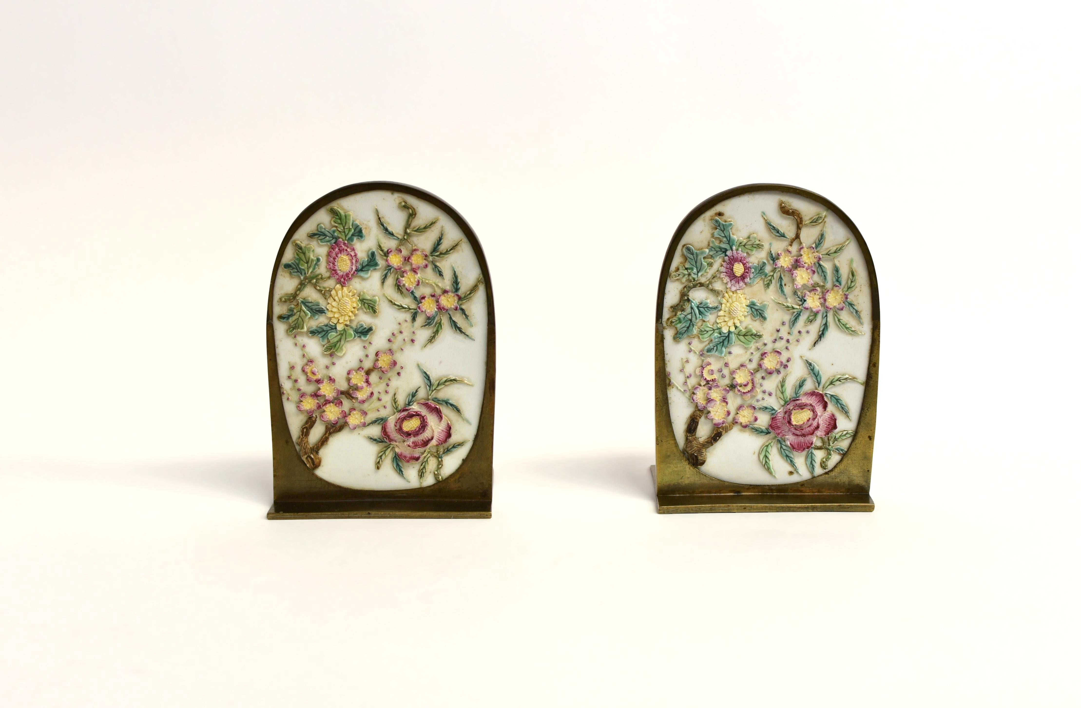 A pair of beautiful solid brass bookends with finely carved porcelain florals. Large porcelain insets in oval form, finely carved in relief with flowers representing four seasons, spring peach blossoms, summer peonies, fall chrysanthemums and