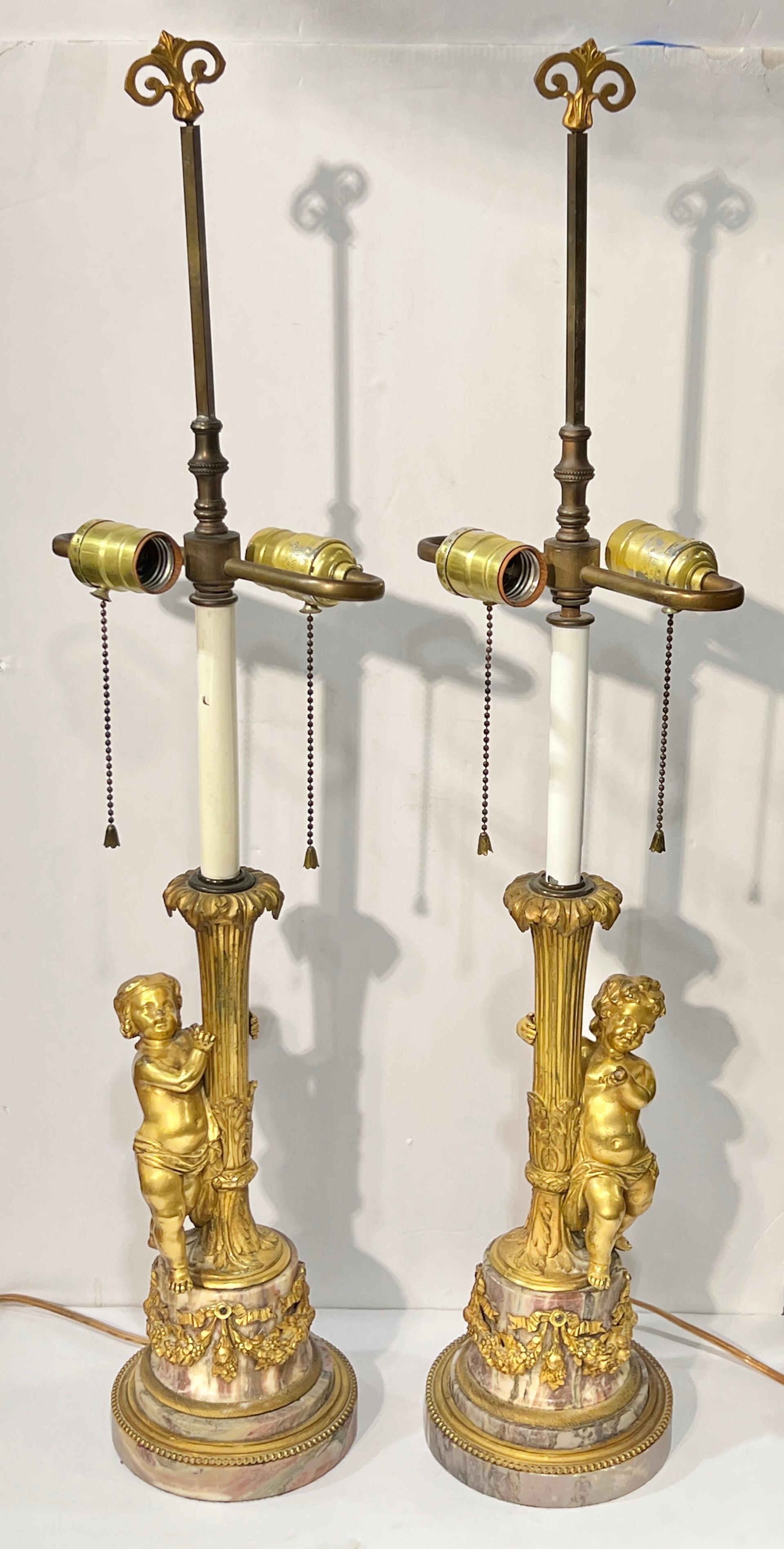 Pair of antique gilt bronze and pink and white variegated marble candlesticks in the French Louis XVI style, finely molded and cast depicting standing cherubs (putti) and floral garlands, later electrified with brass hardware and two sockets.  29