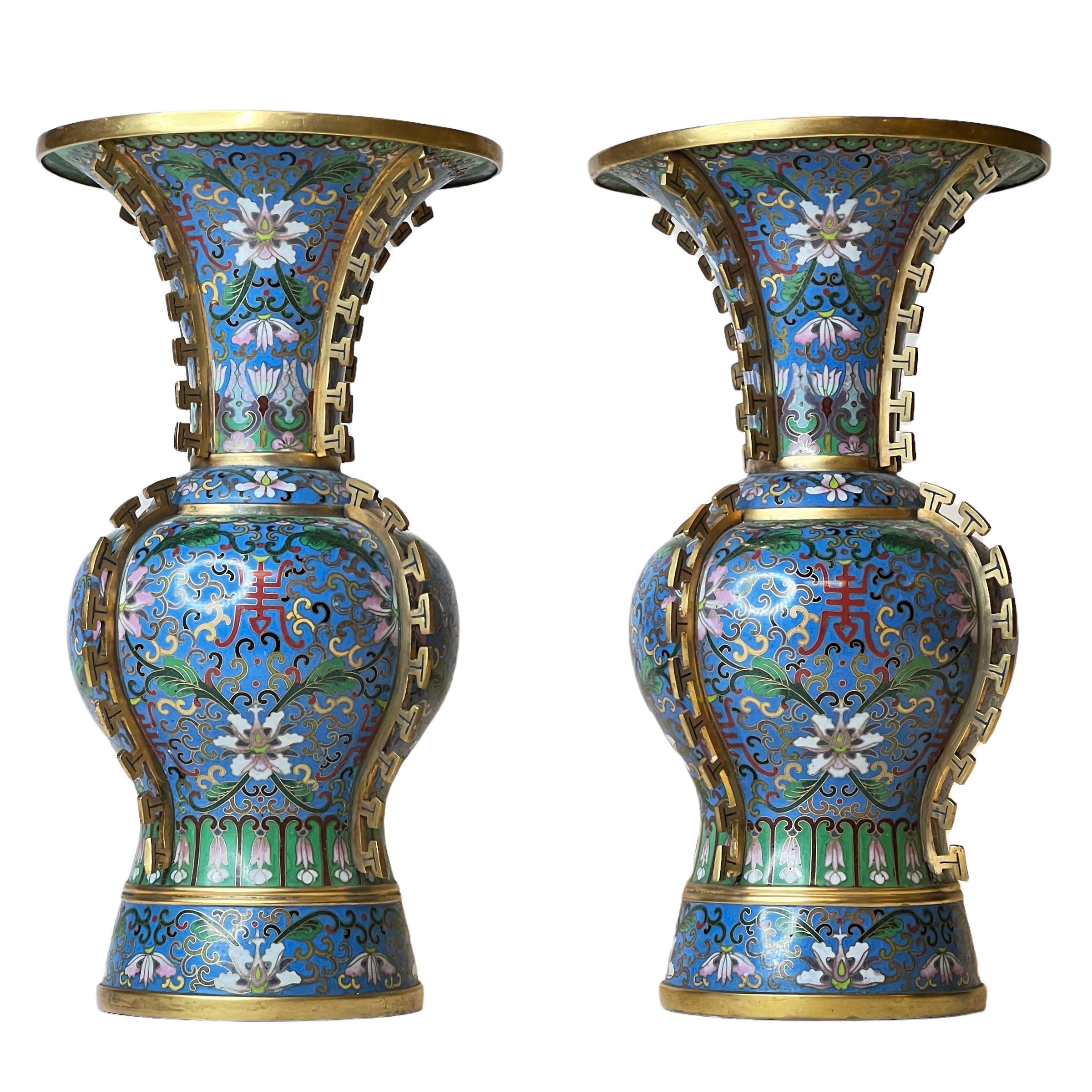 Paar chinesische Cloisonné-Emaille-Vasen mit floralen Motiven auf blauem Grund und vergoldeten Beschlägen, die stilisierte Rückenflossen eines Drachens darstellen.