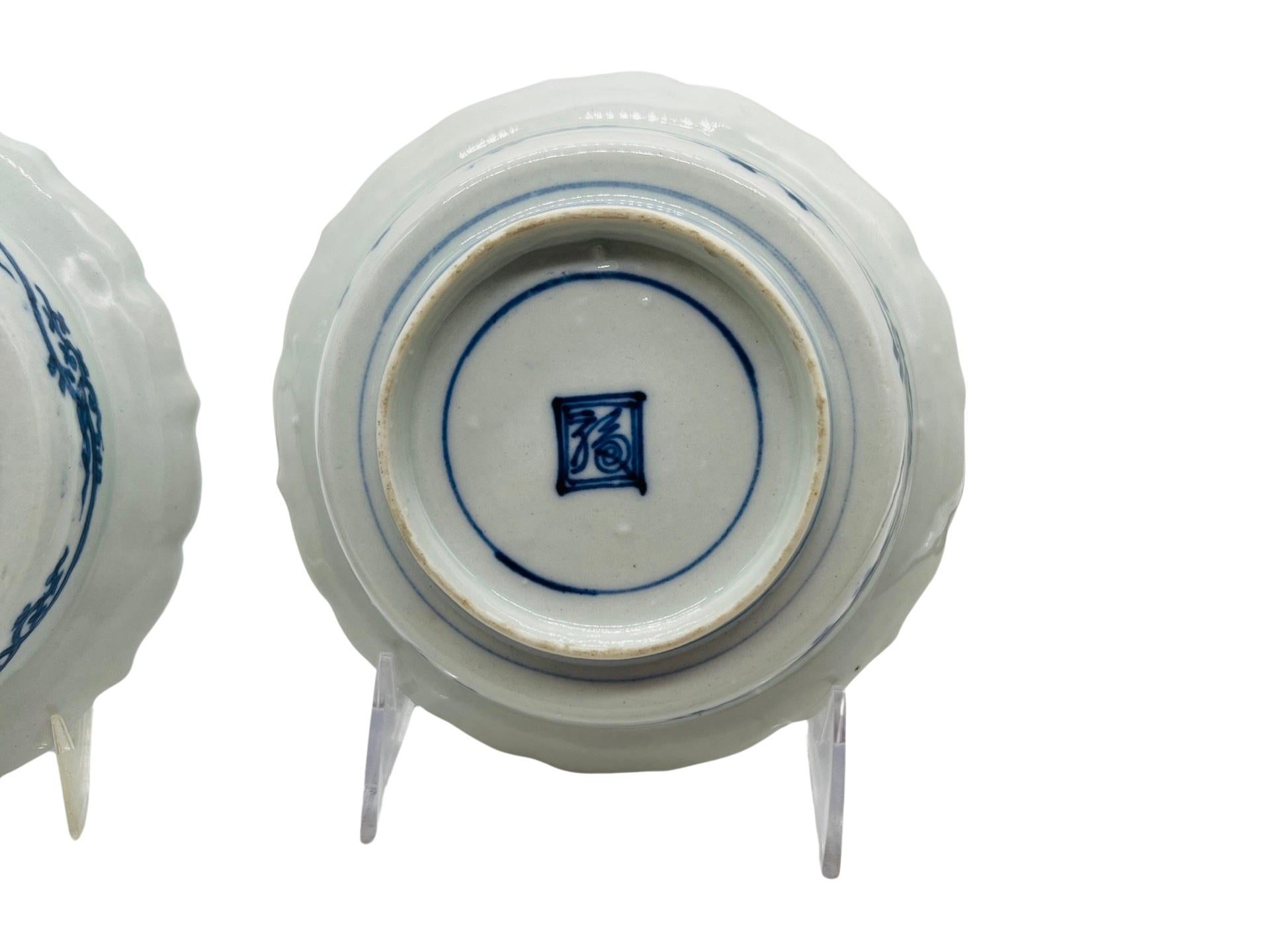 Chinois, 20e siècle. 
<br>Paire de bols festonnés bleus et blancs avec des scènes figuratives à l'intérieur et entourés de motifs feuillus. 
<br>Marqué sur la face inférieure. 
<br>Approx : 5.875
